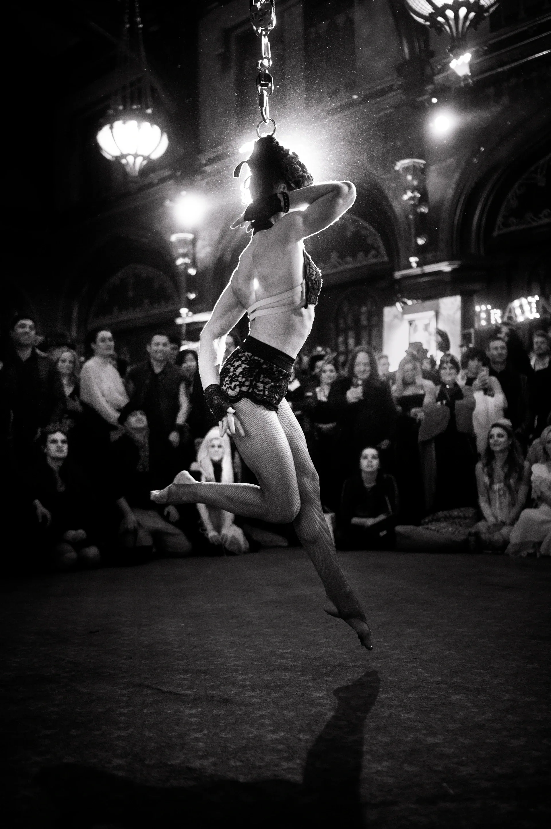 Costumed performer balances on one leg before a seated crowd.