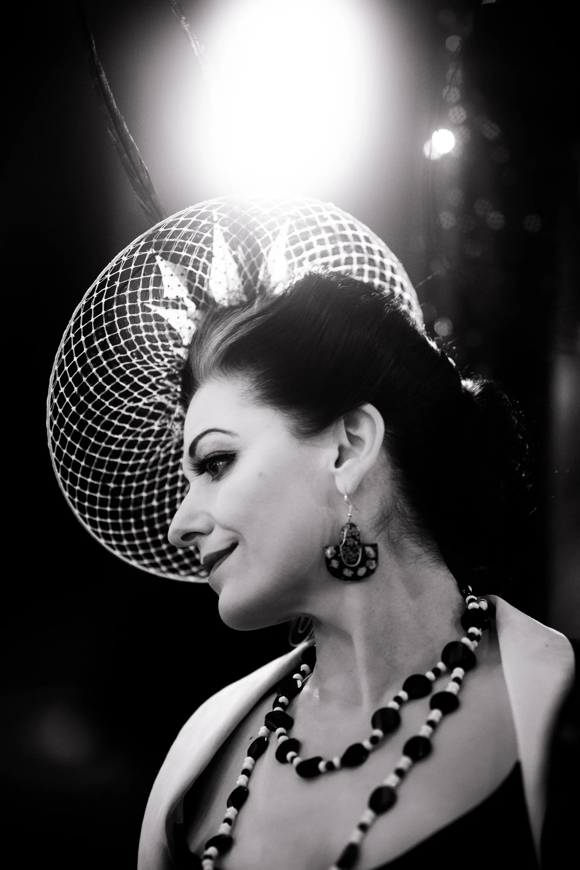 Performer wearing a circular netted headpiece and necklace looks to the side.