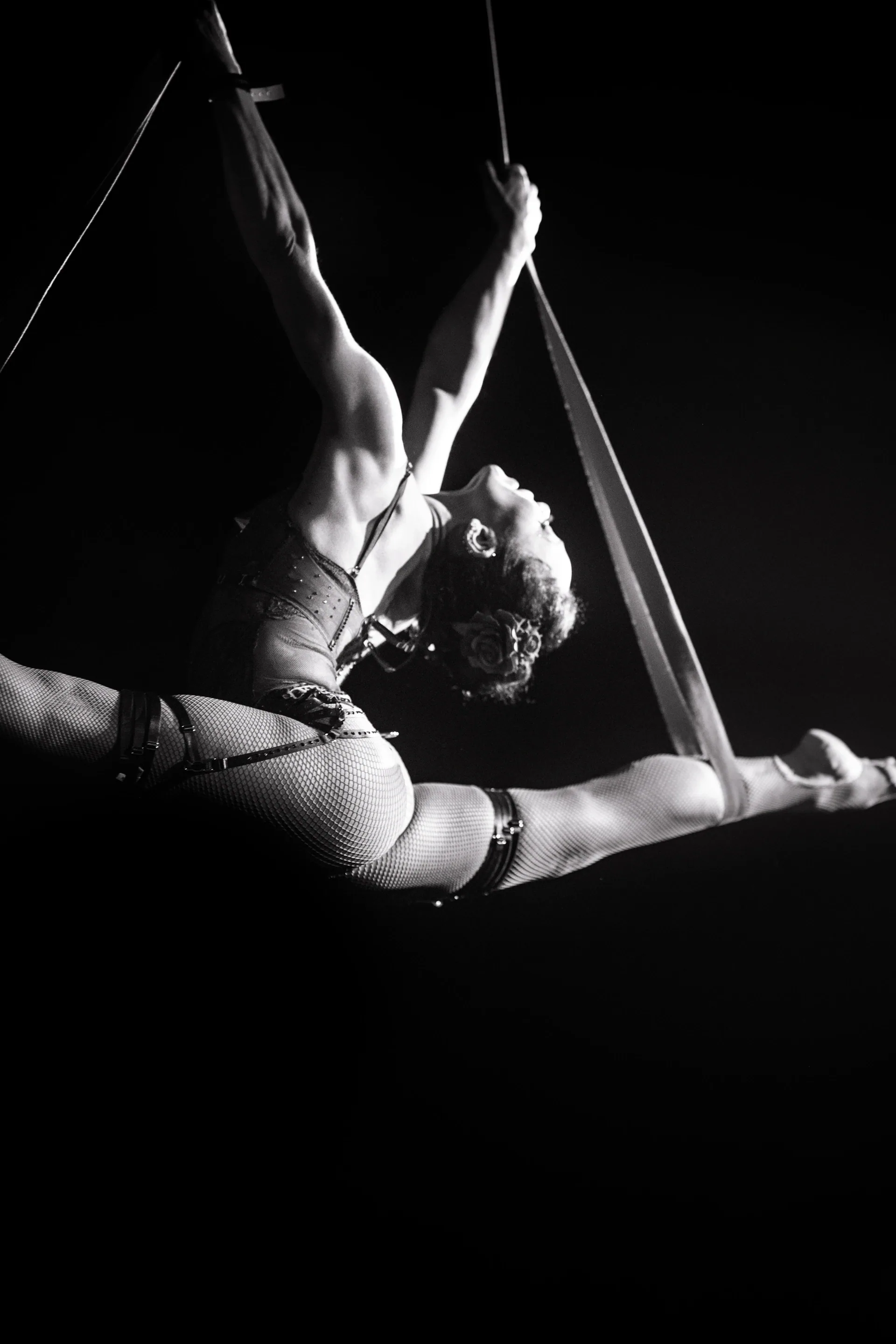 Aerialist arches backward while suspended from a trapeze-like apparatus.