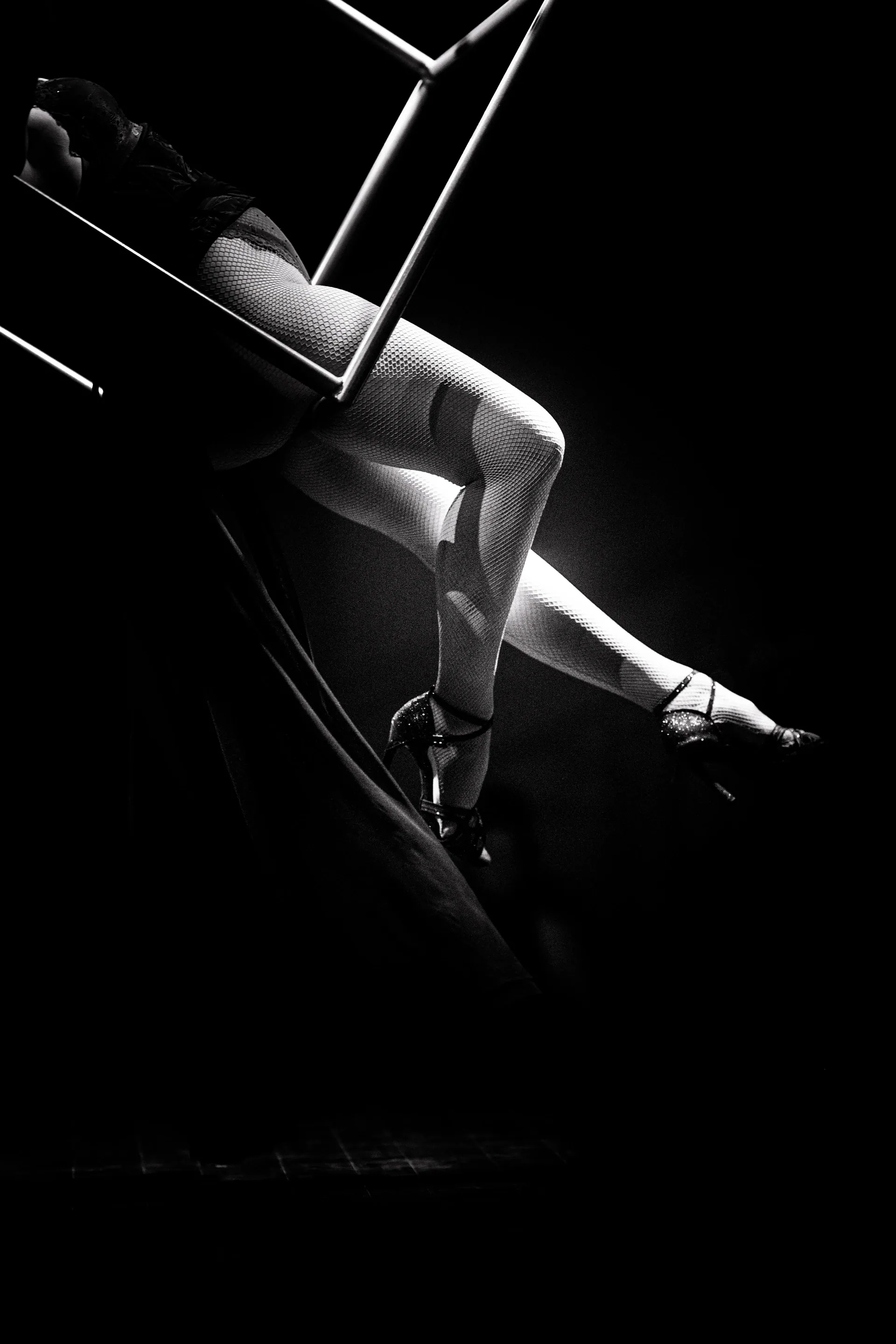 Aerialist reclines inside an angled metal frame with one leg extended.