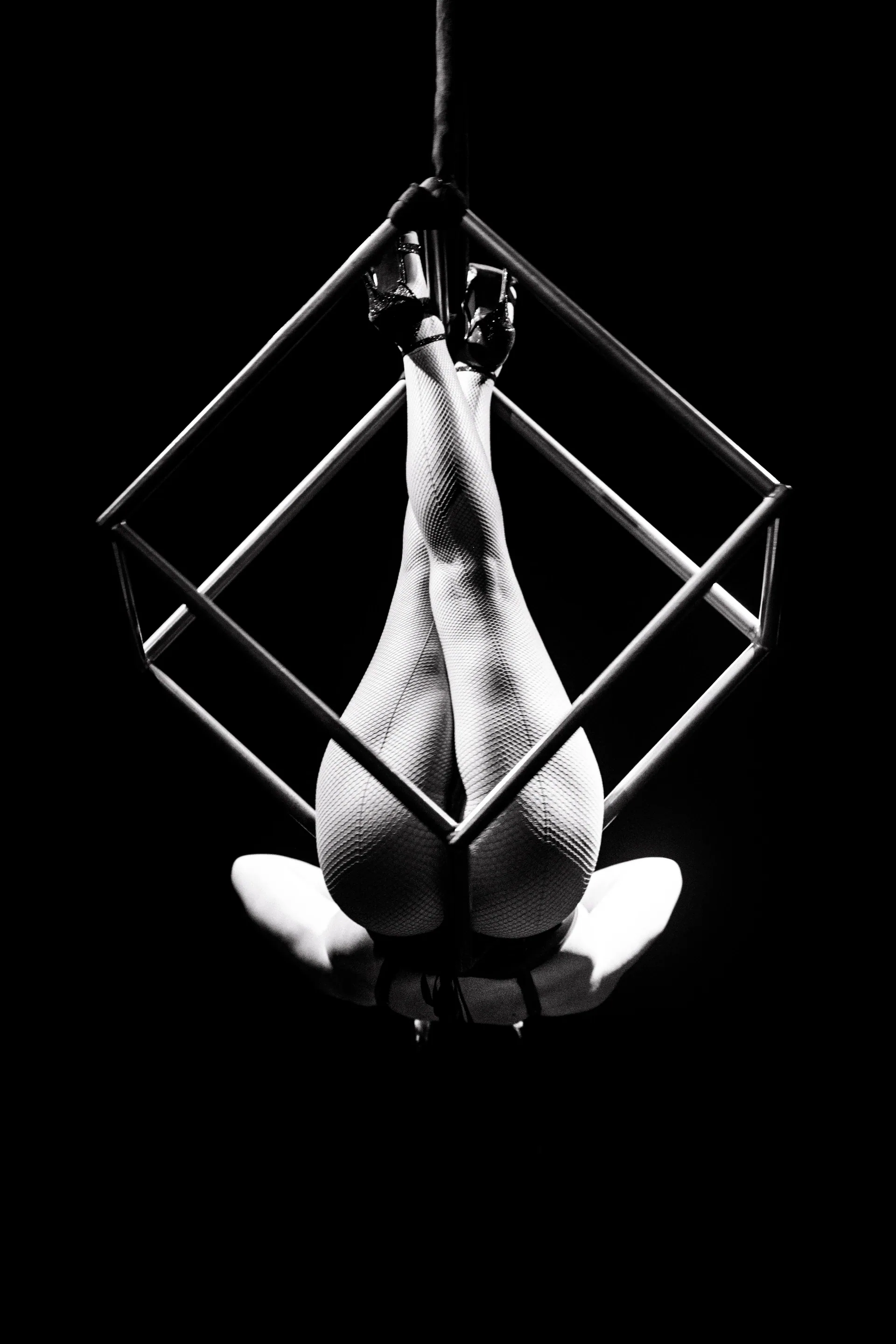 Inverted aerialist hangs inside a diamond-shaped metal frame.