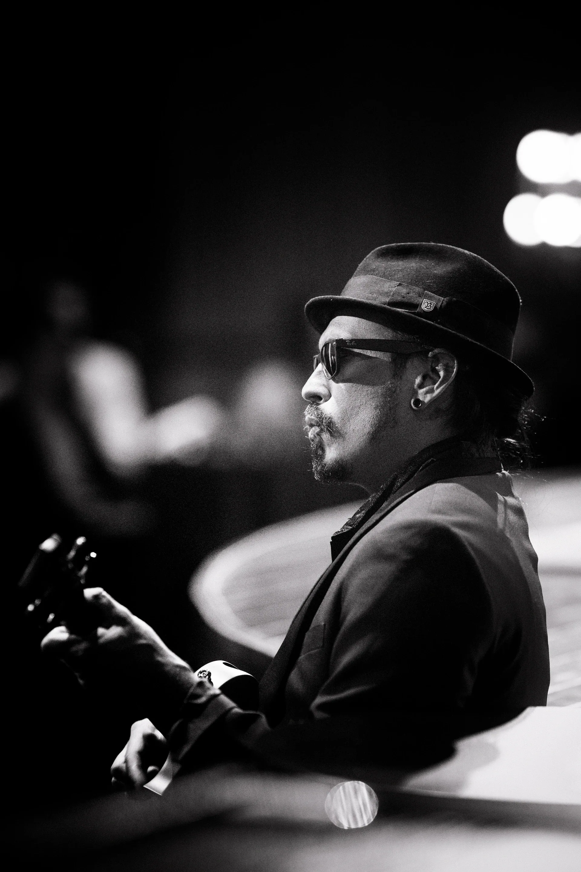 Musician in a hat and glasses plays guitar while seated.