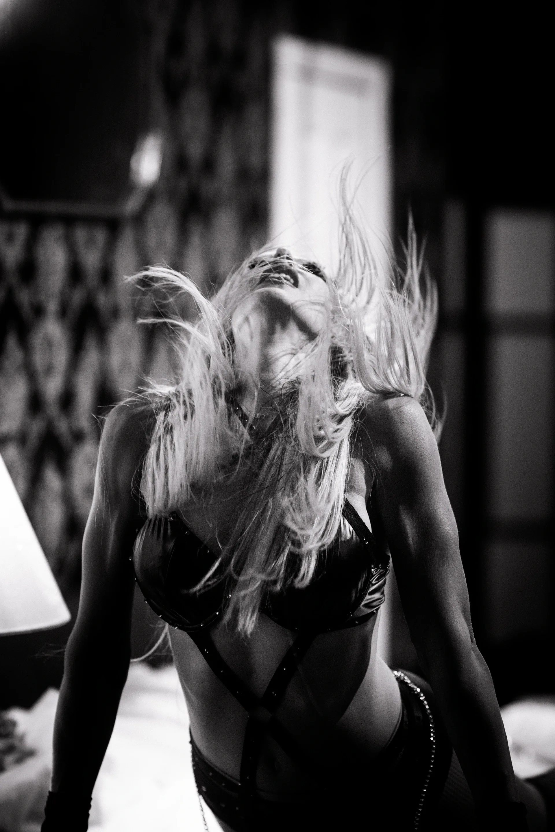 Long-haired performer kneels near a bed with the head tilted back.