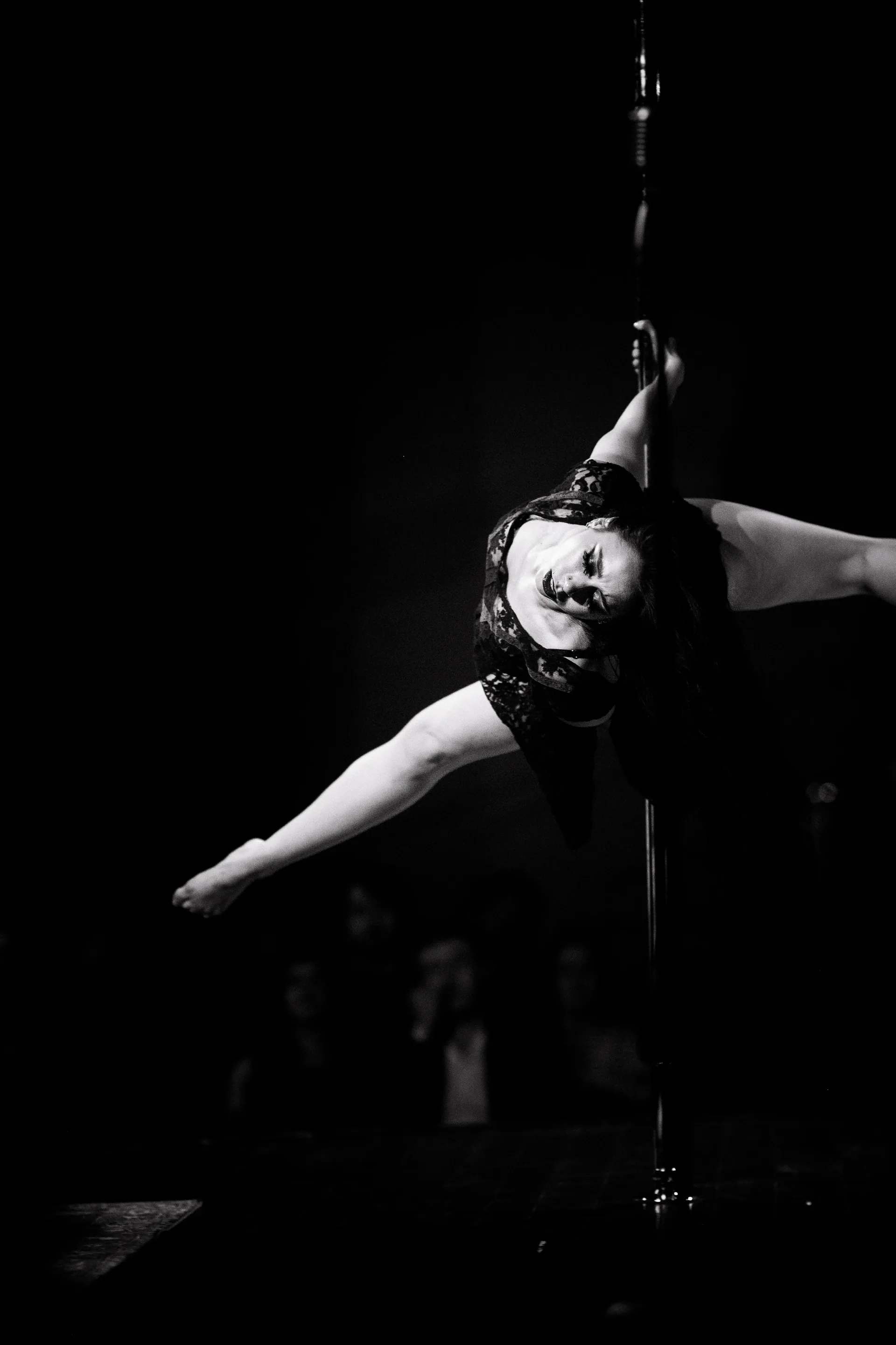 Aerialist extends one arm while suspended from a vertical strap.