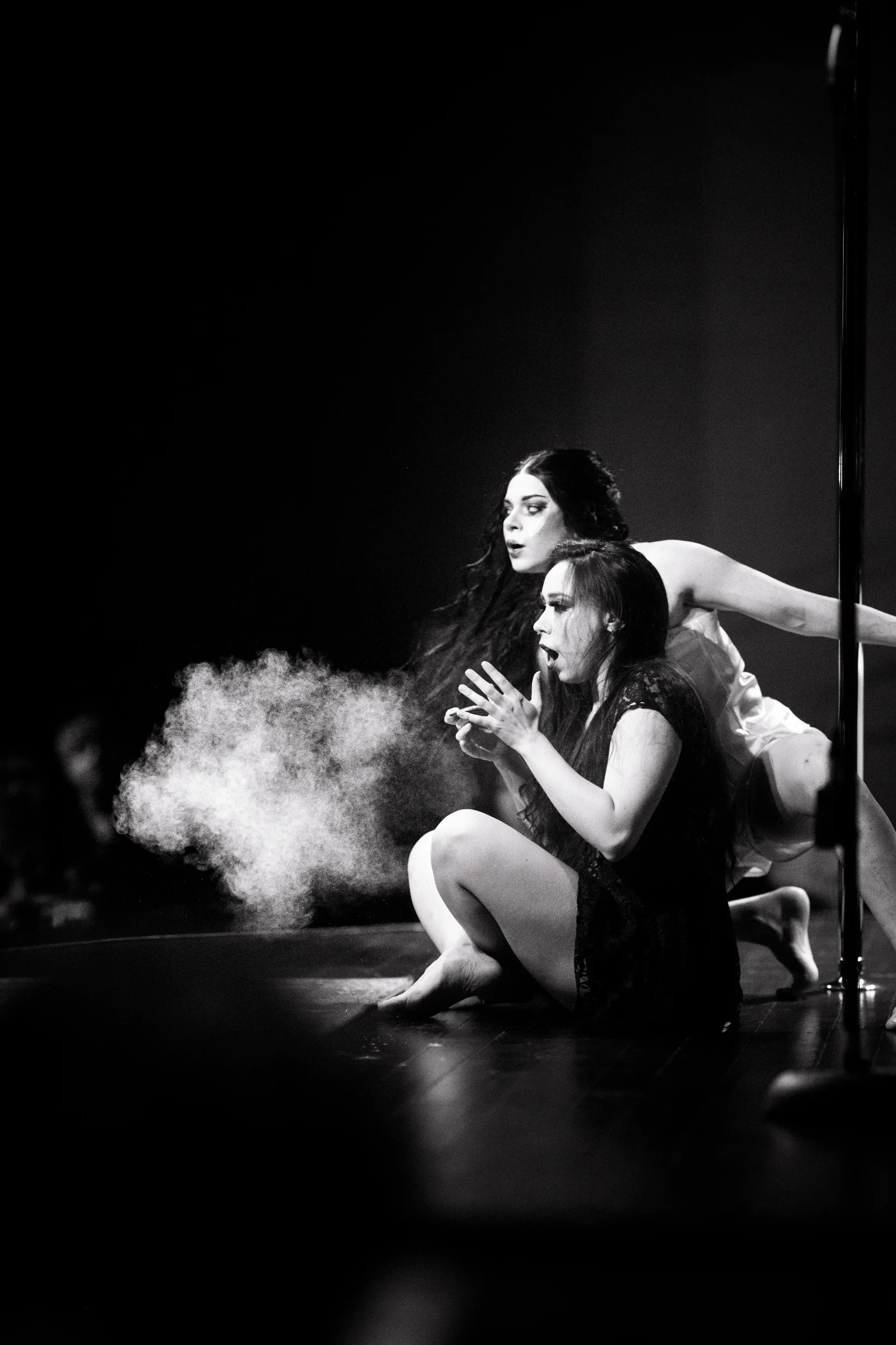 Seated performer holds both hands near the mouth as smoke drifts nearby.