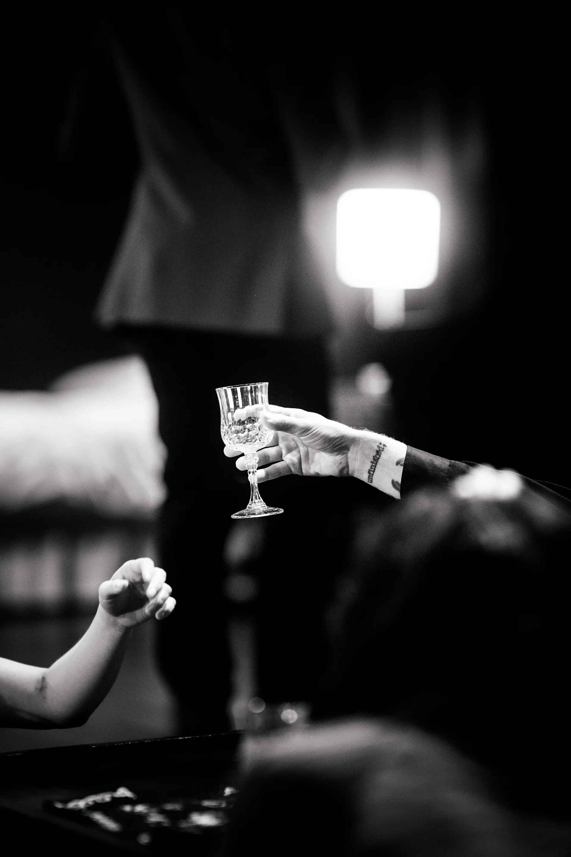 A hand holds a stemmed glass beneath a small spotlight.
