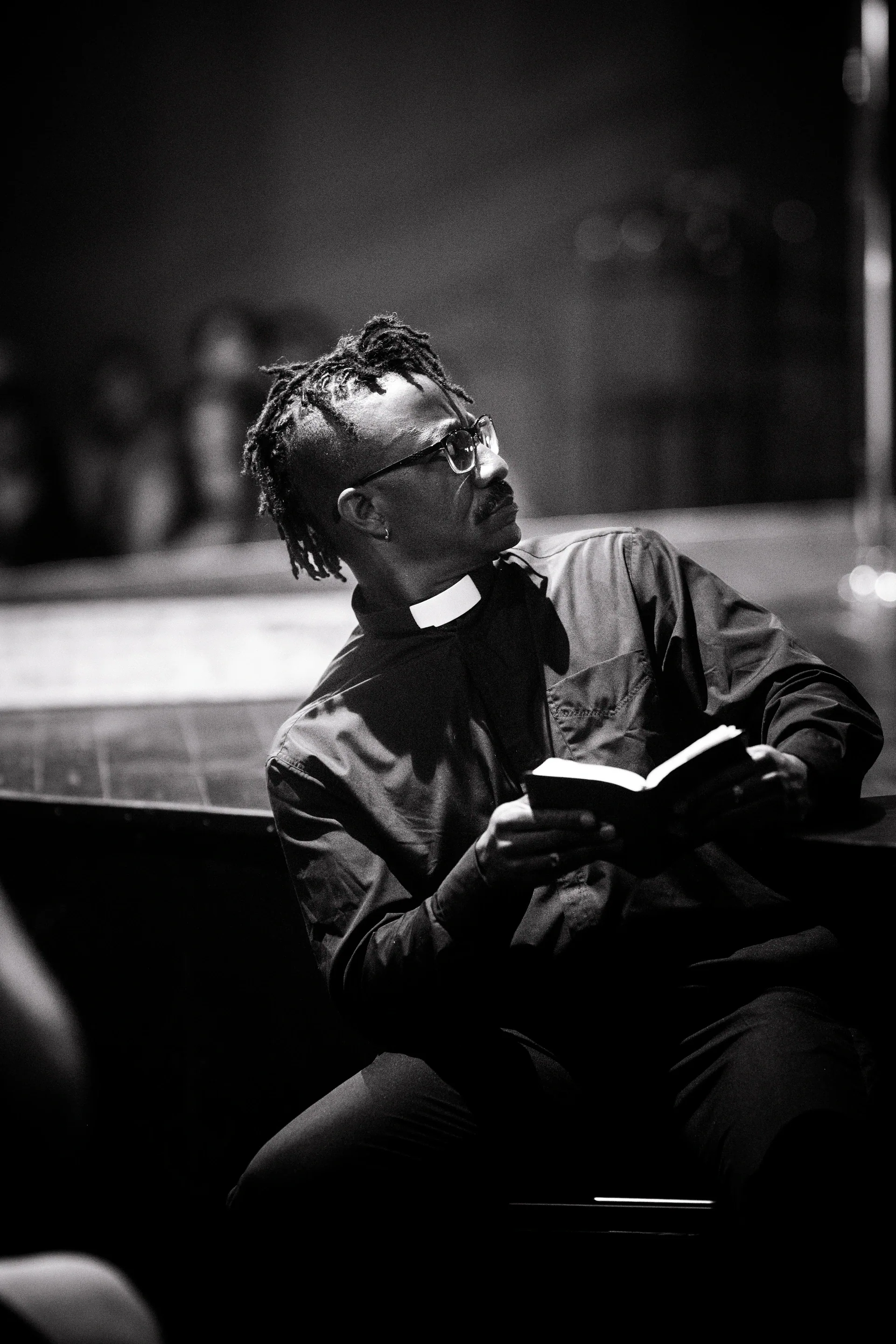 Person wearing glasses reclines while reading an open book.
