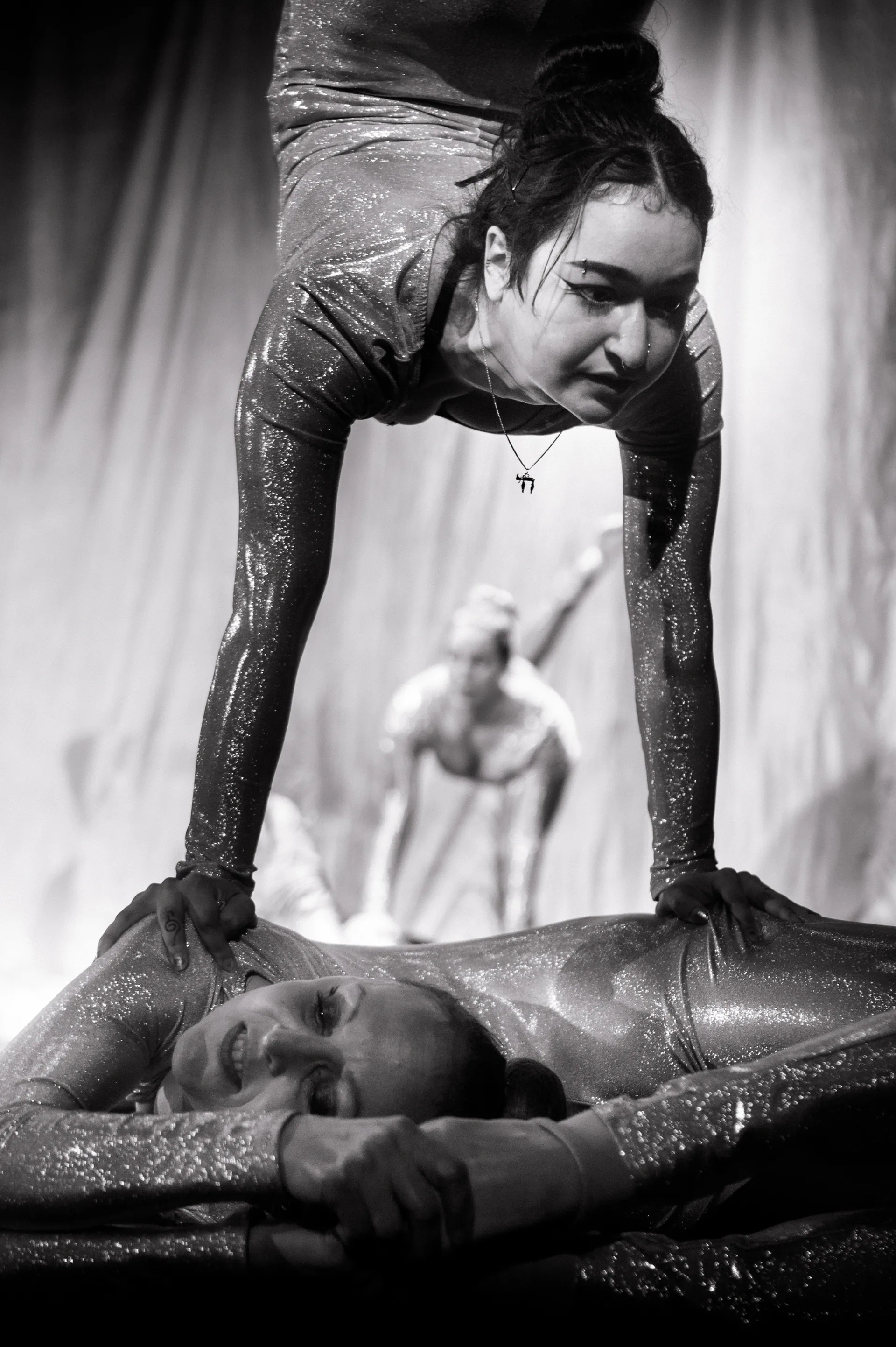 Contortionist leans over a performer lying on a padded platform.