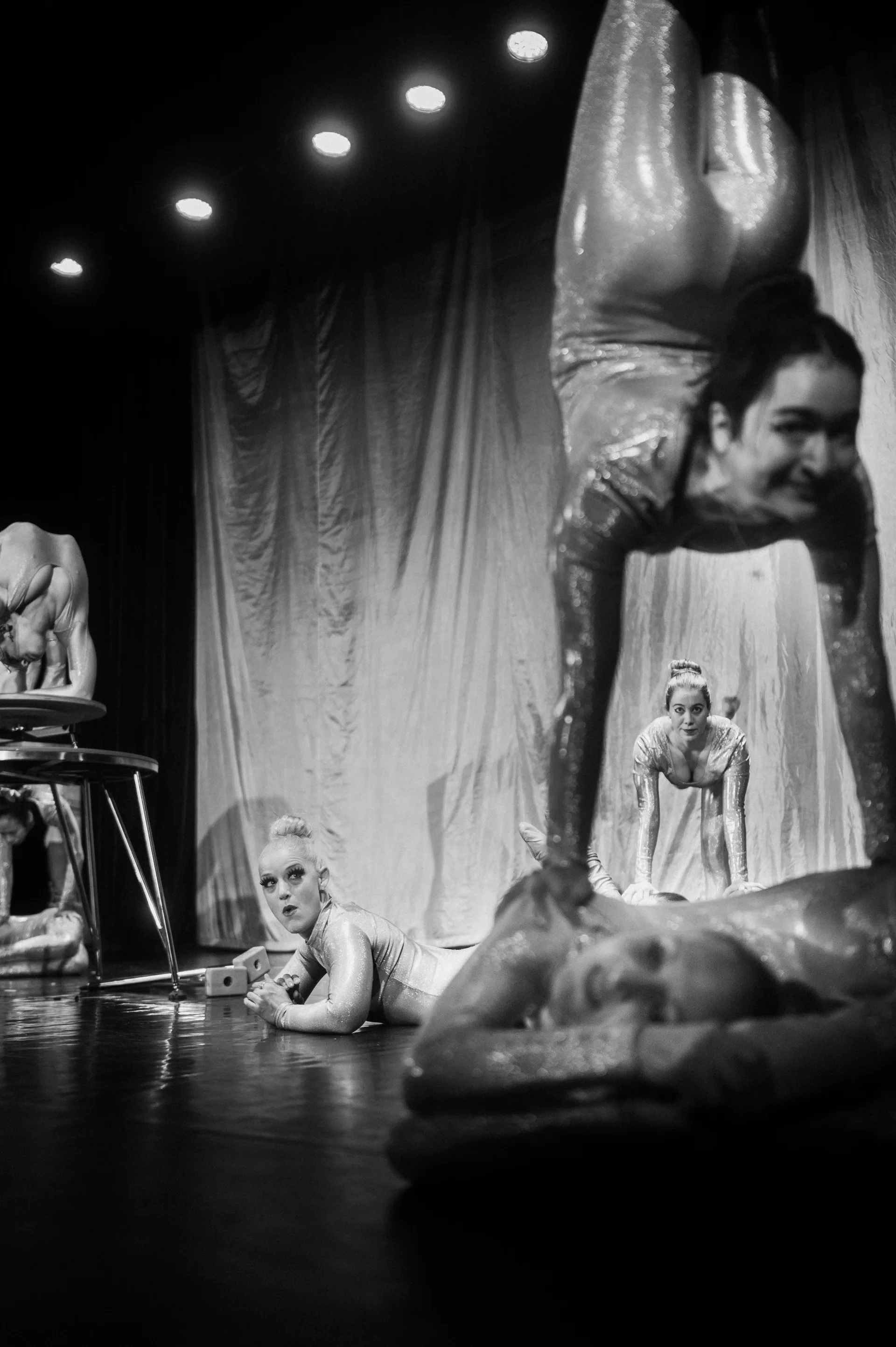 Contortionist holds a deep backbend over another performer on a platform.