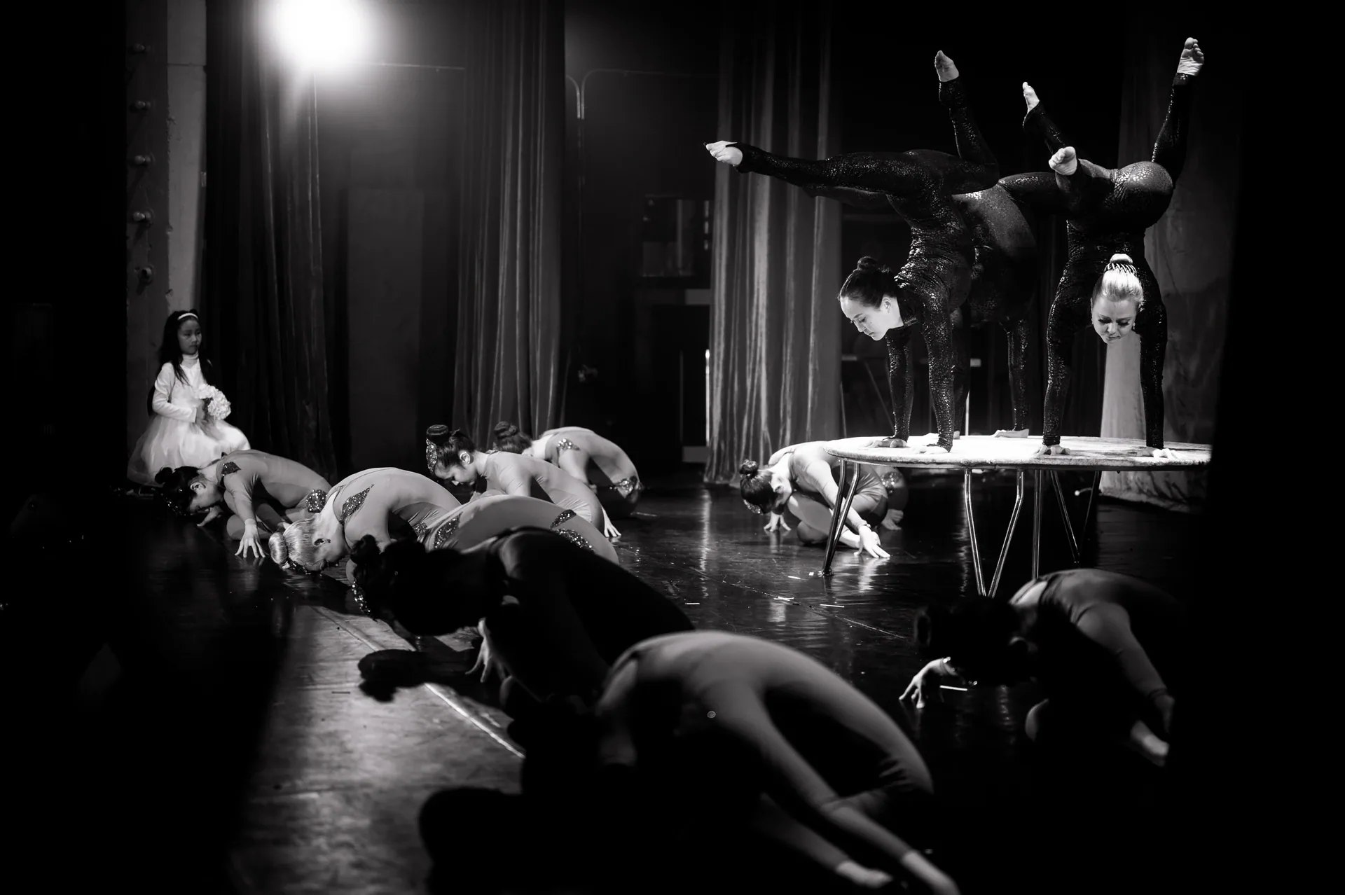 Group crouches onstage while one performer balances above them on a platform.
