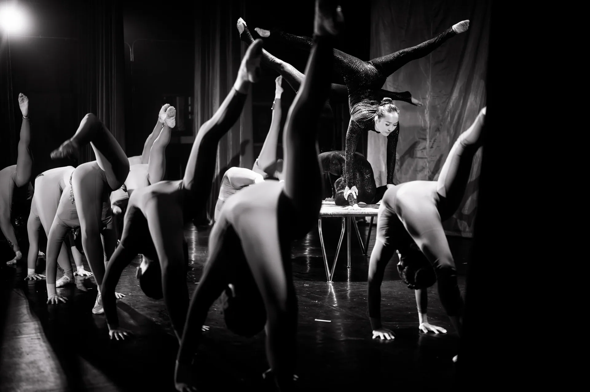 Row of performers holds backbends and handstands around a raised platform.