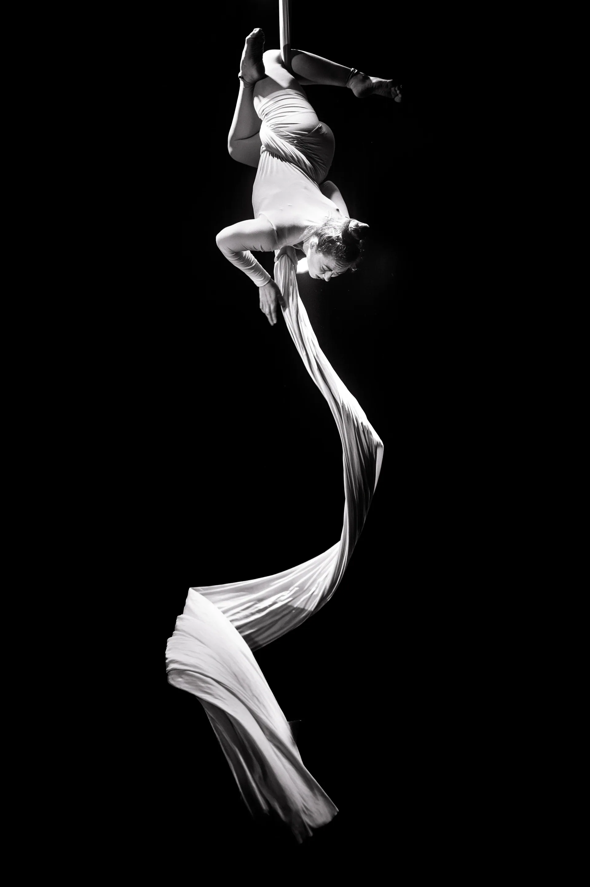 Aerial performer hangs upside down in flowing white silks.