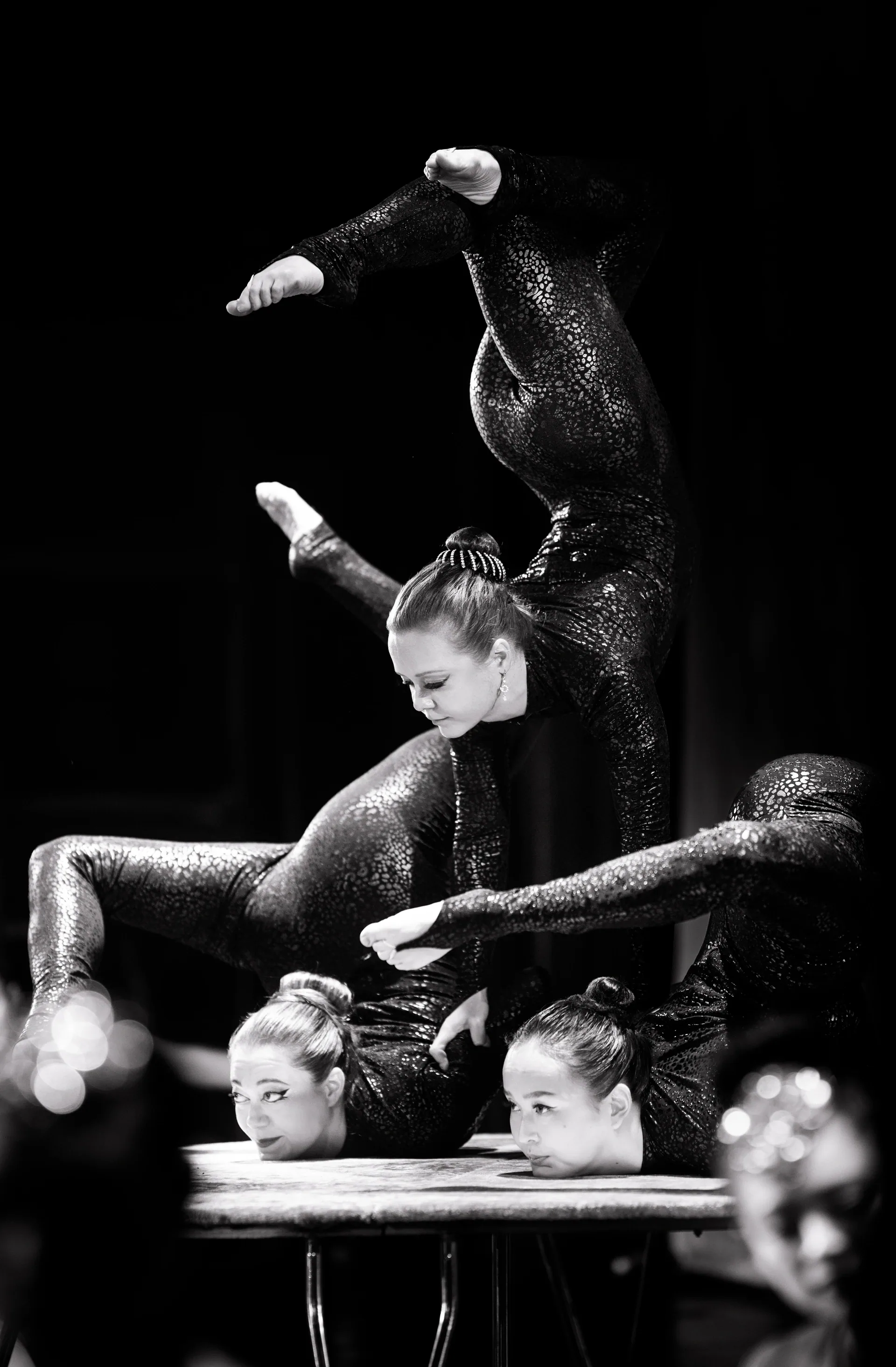 Two contortionists hold a stacked pose with legs curved overhead.