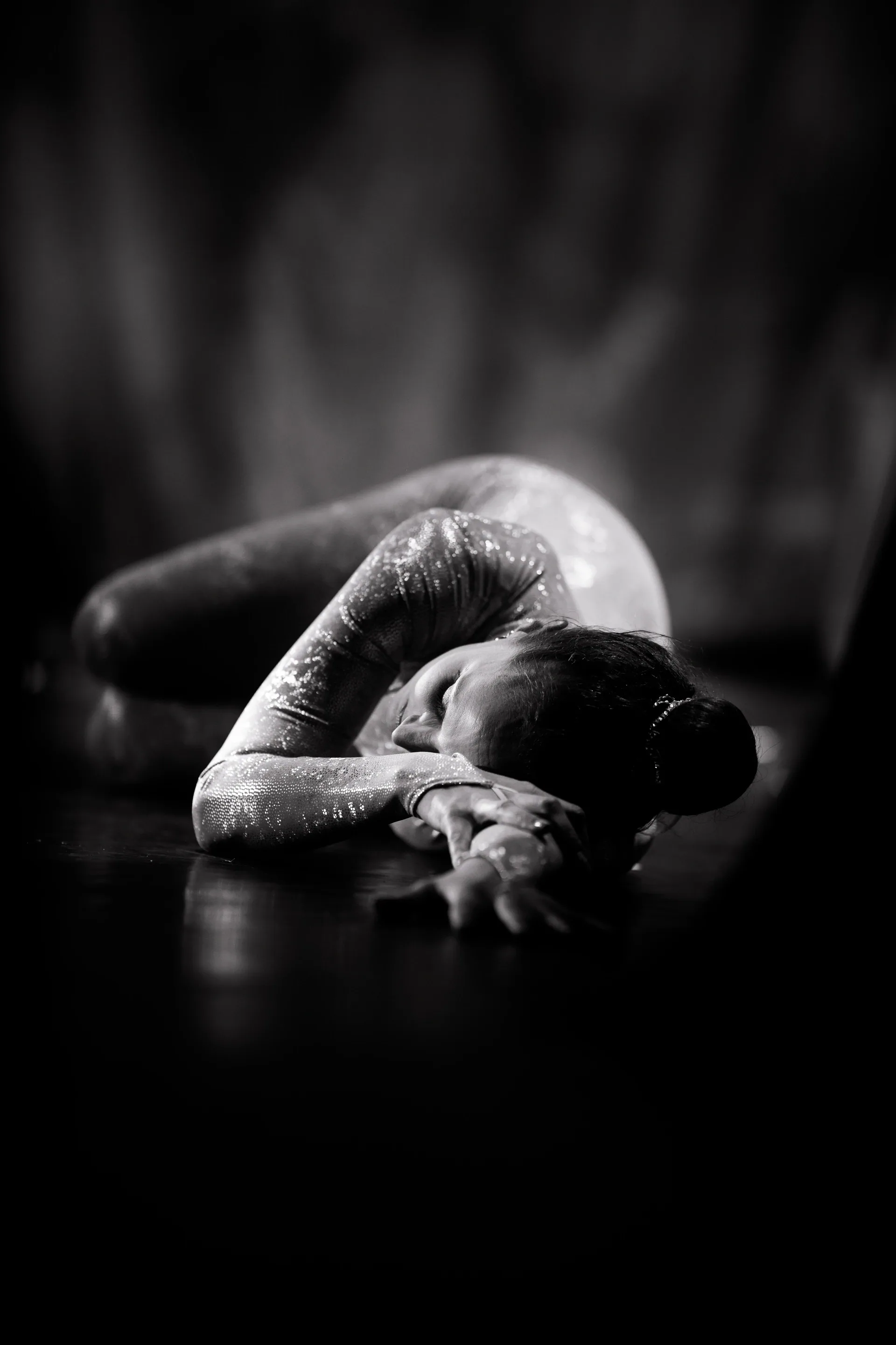 Contortionist folds backward on the floor with legs over the head.