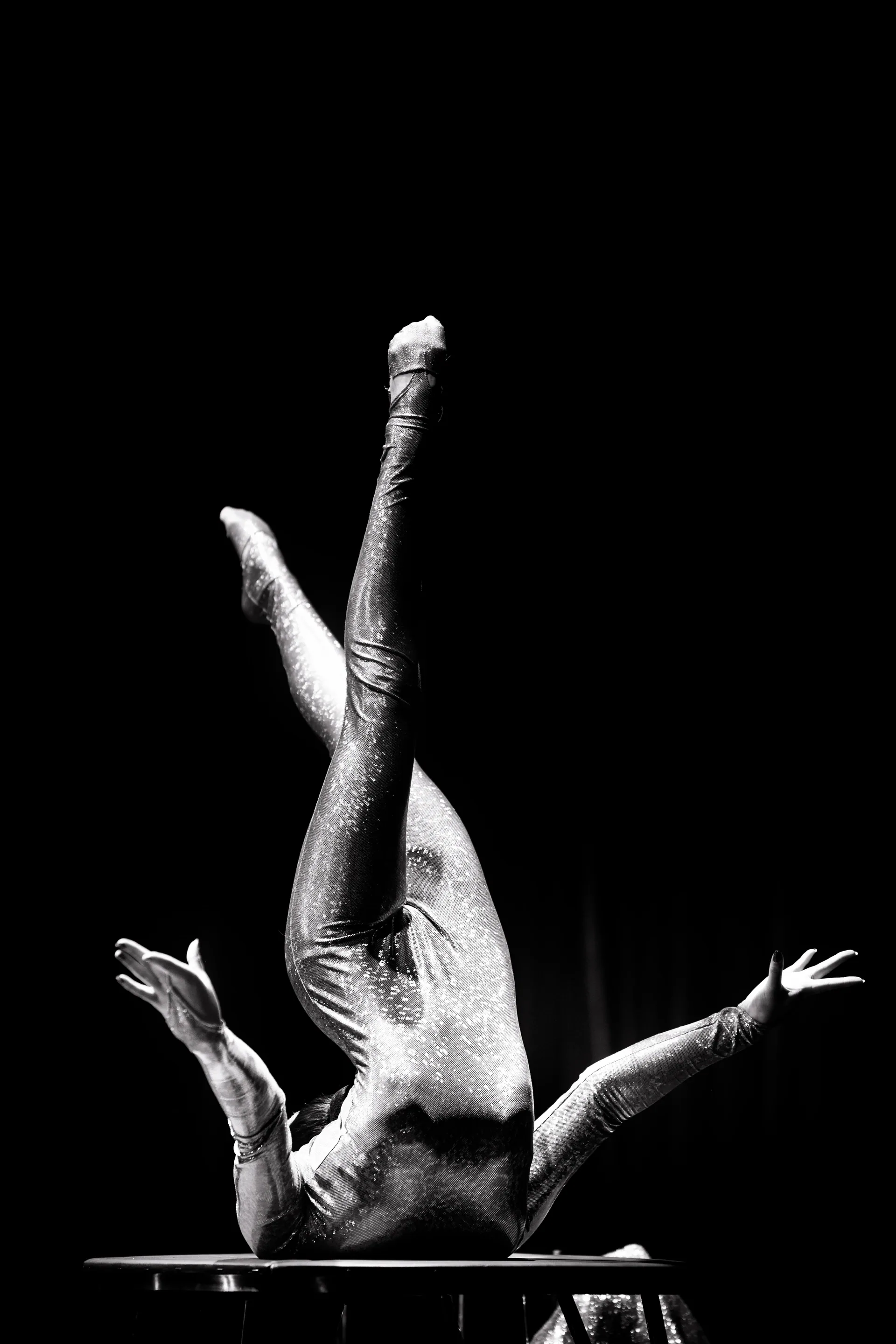 Performer holds a one-arm handstand with legs split above a small table.
