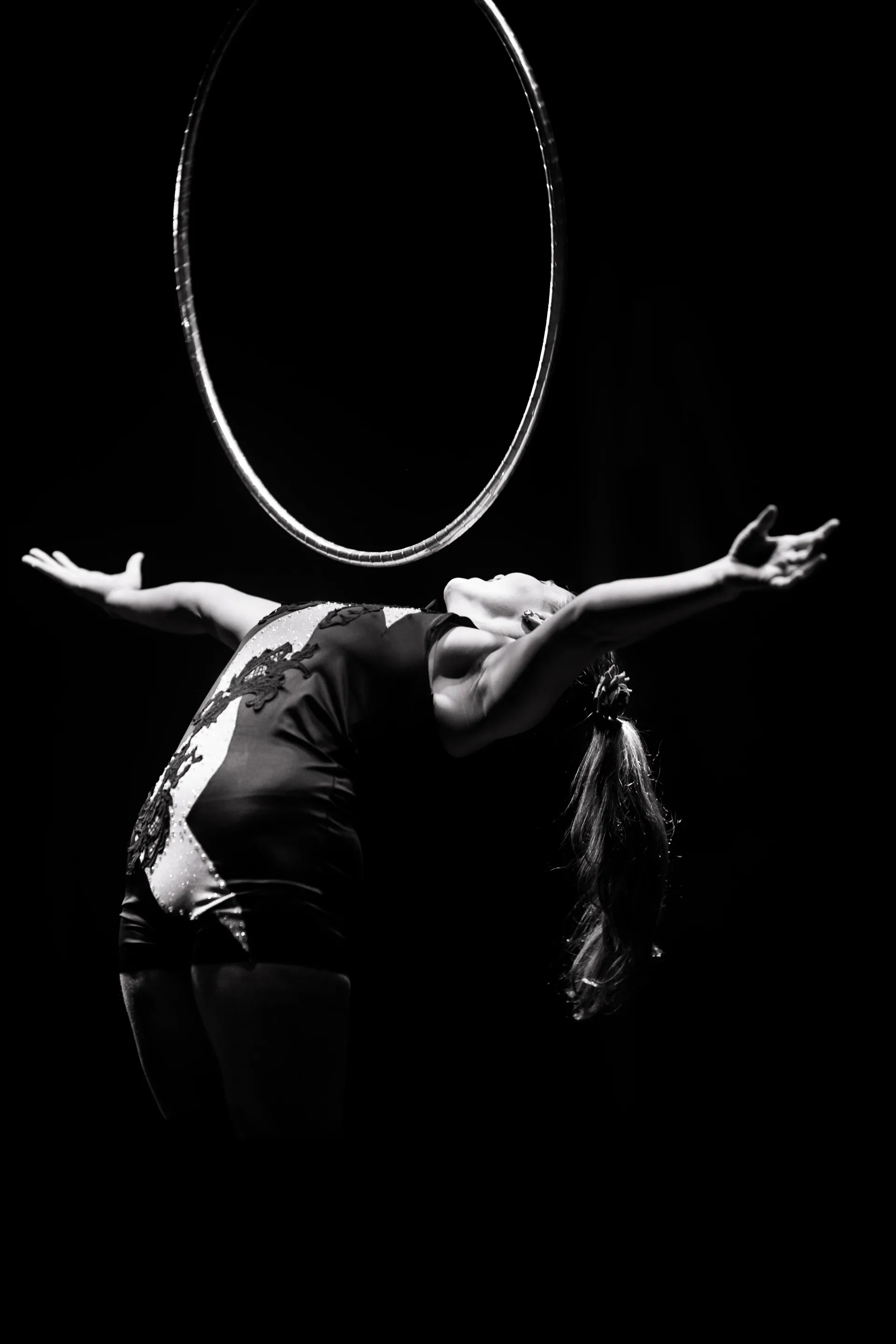 Performer arches backward beneath a suspended hoop with arms extended.