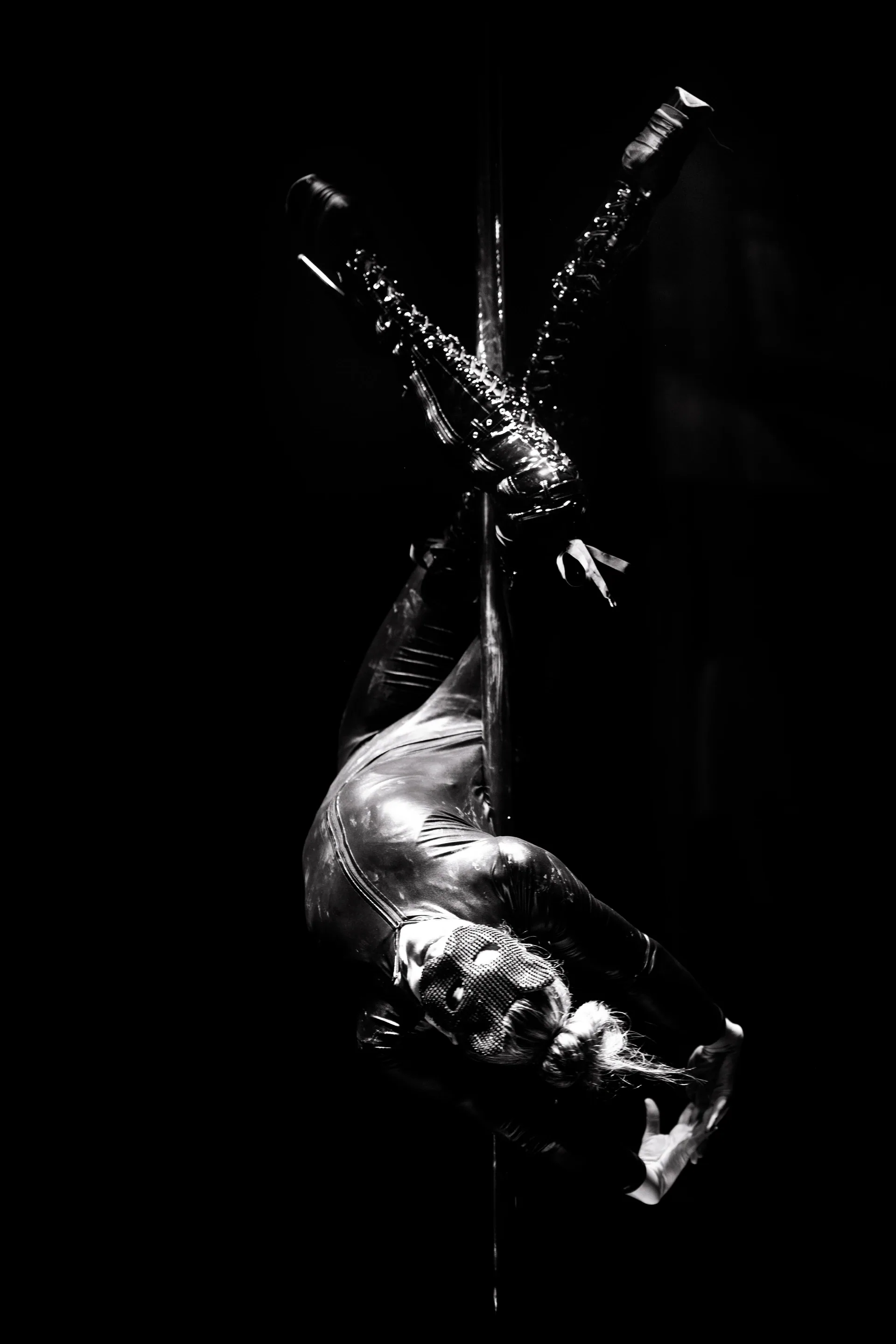 Aerialist hangs upside down from straps with legs spread above.