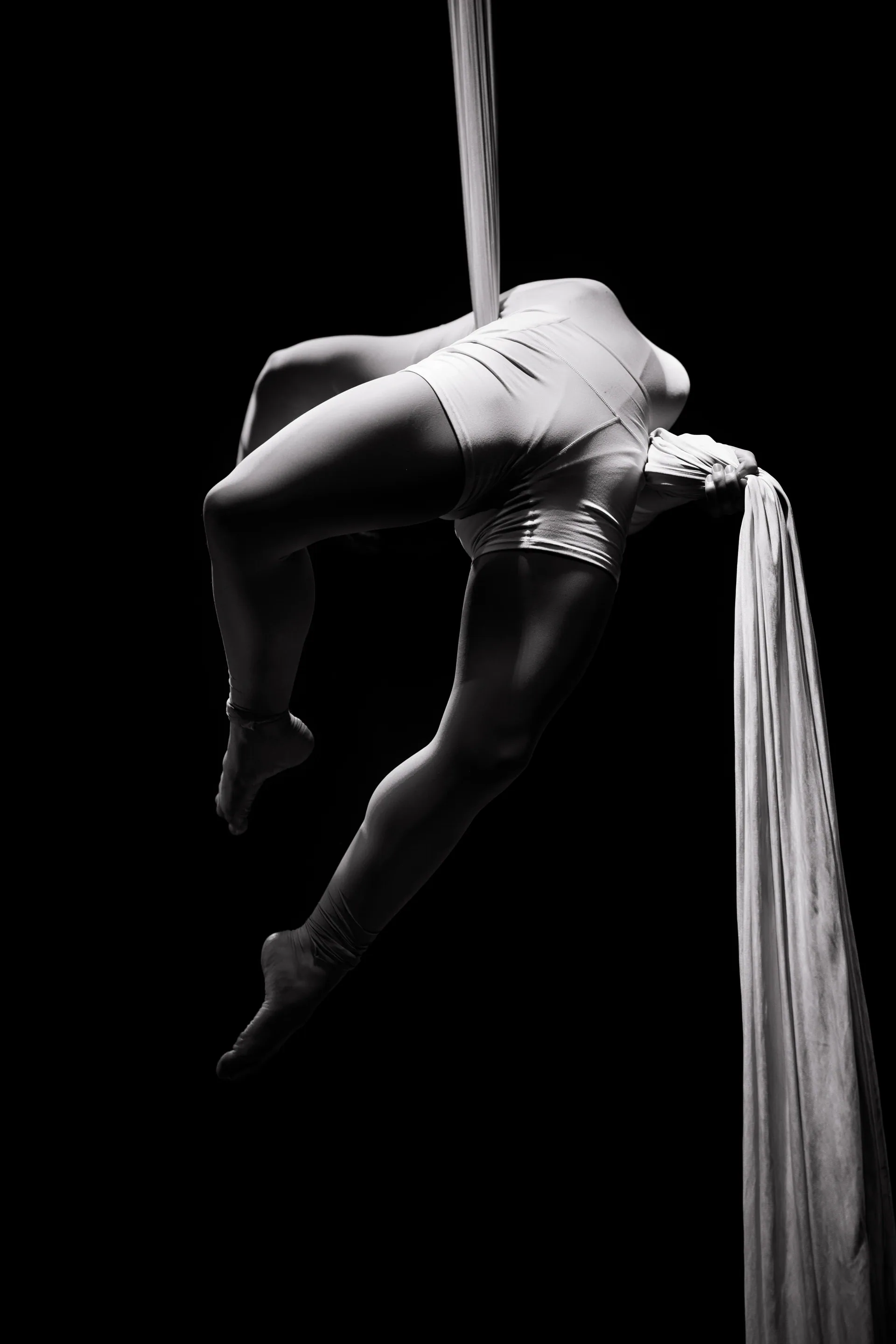 Aerialist arches backward while wrapped in white silks.