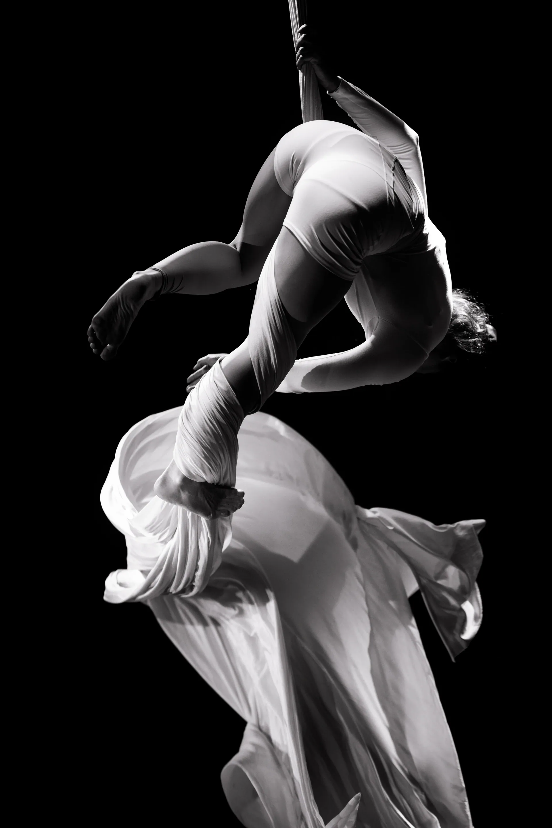Aerialist curls upside down around flowing white silk.