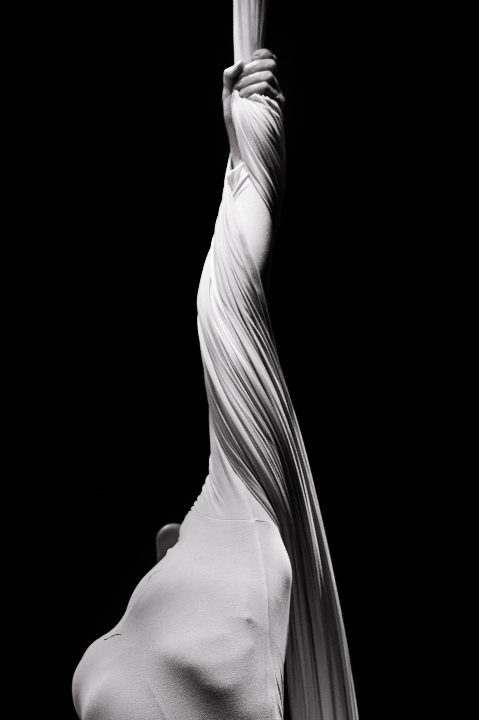Aerialist hangs fully enclosed inside a column of white silk.