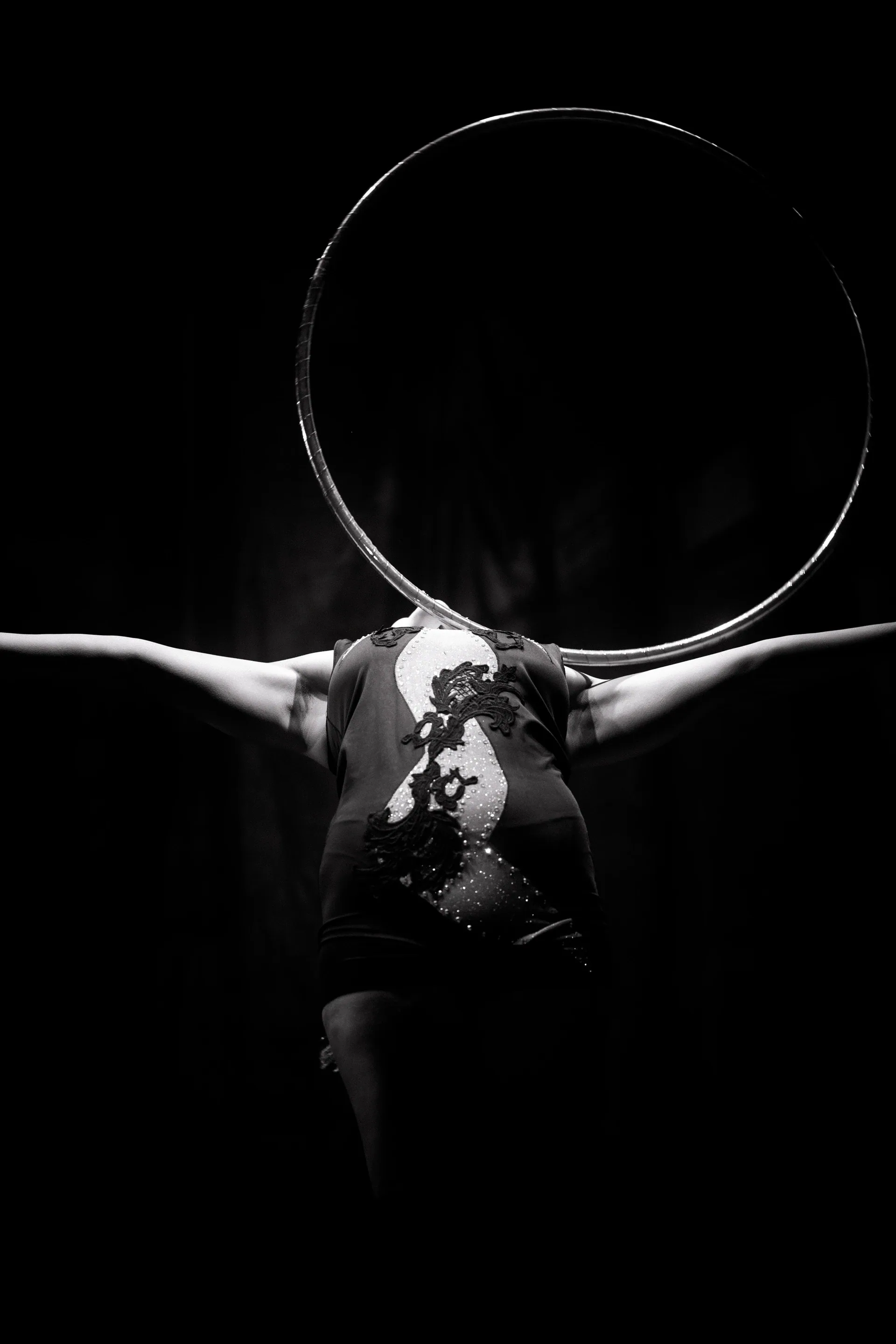 Performer arches backward beneath a large hoop with both arms extended.