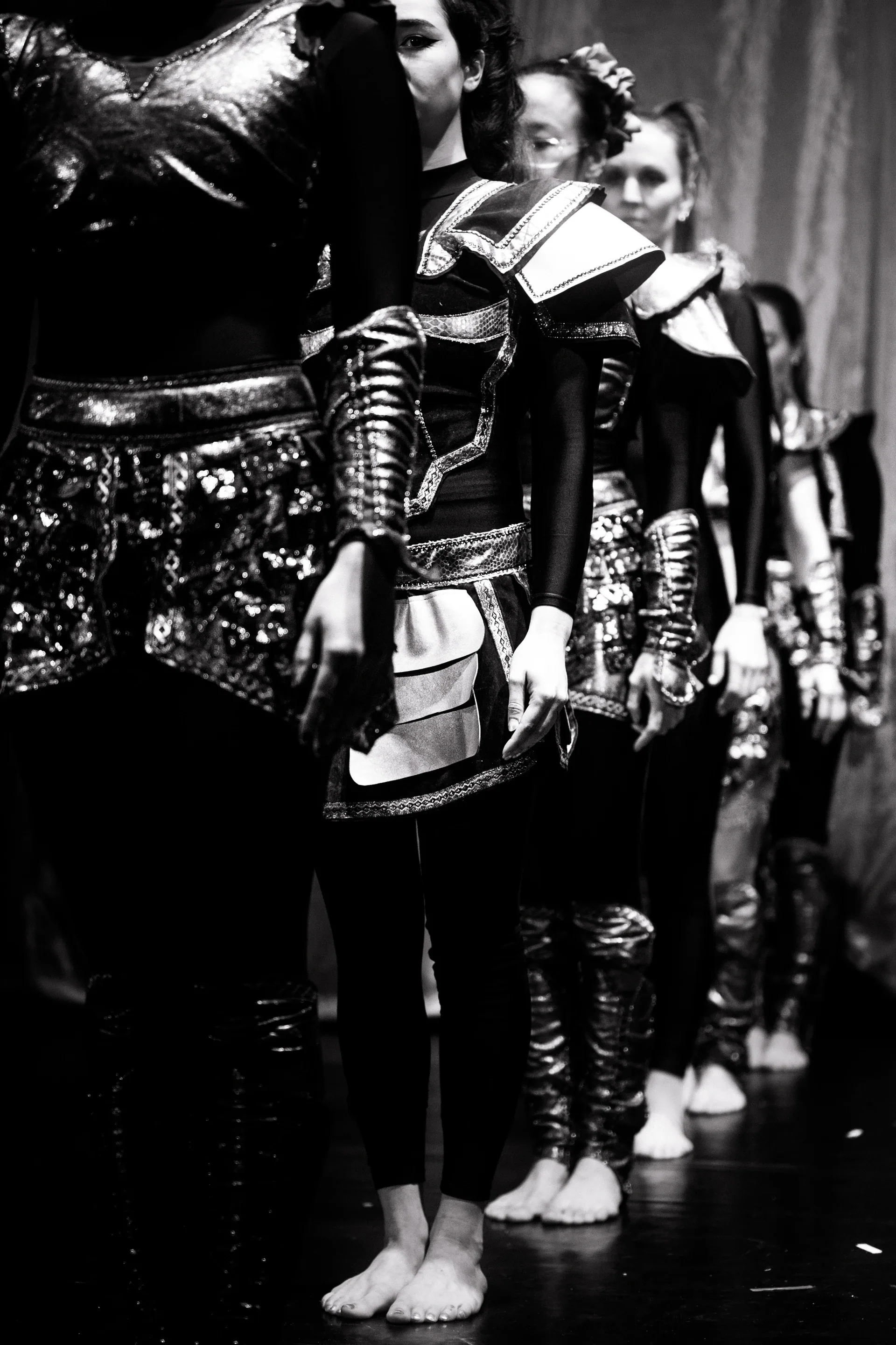 Line of performers in structured dark costumes stands backstage.