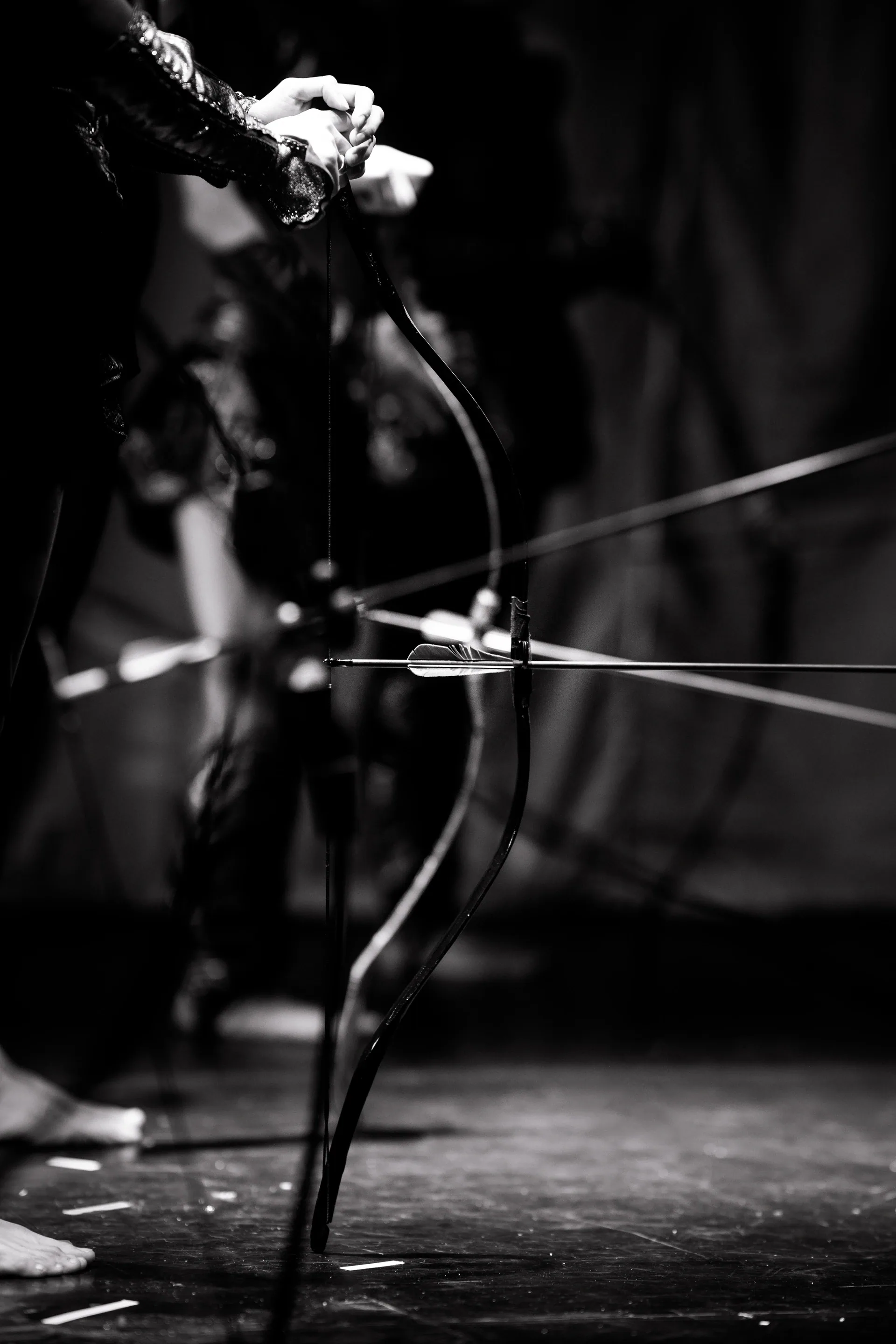 Close view of hands holding a bow with several arrows resting across it.