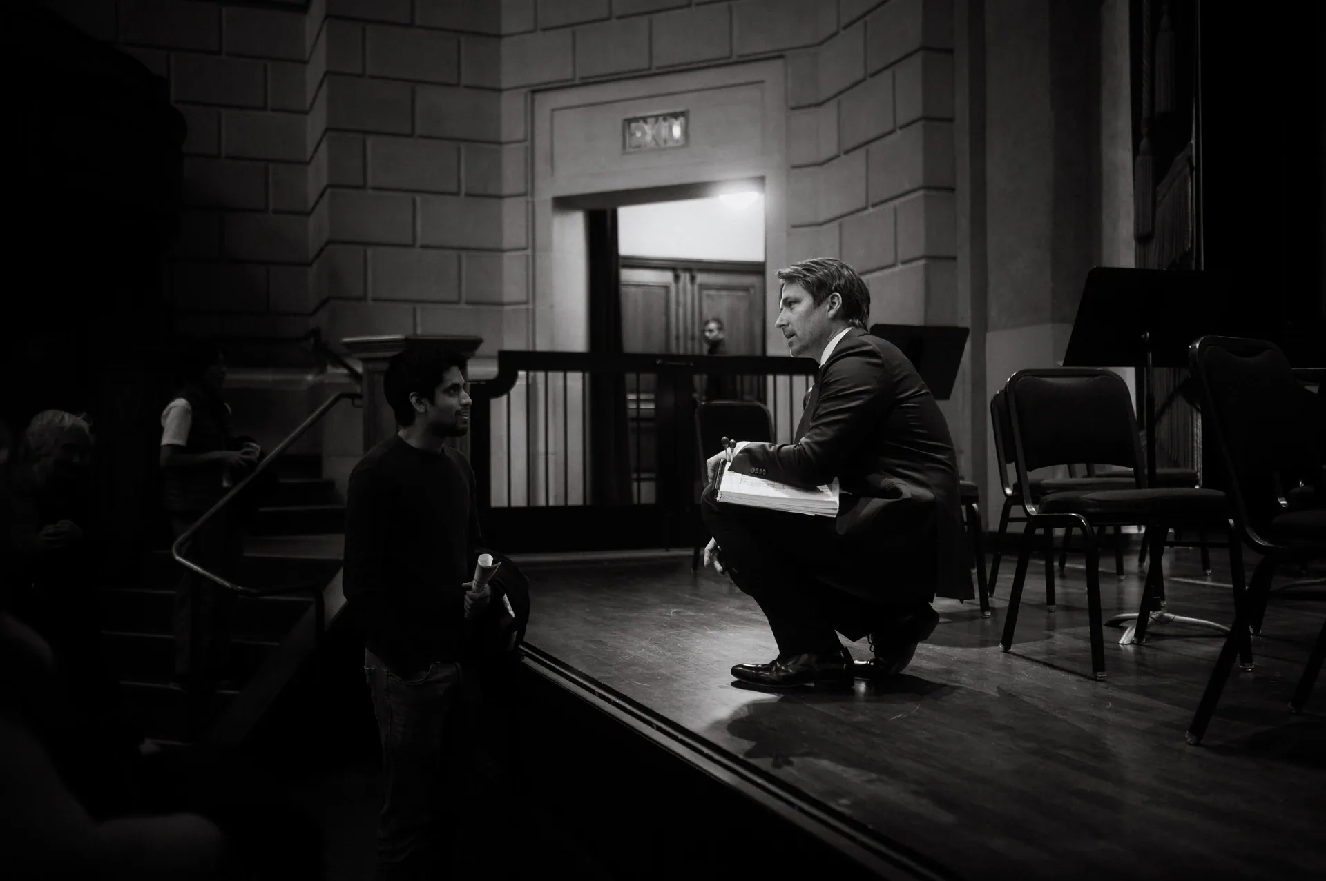 Two people crouch beside empty chairs near the edge of the stage.