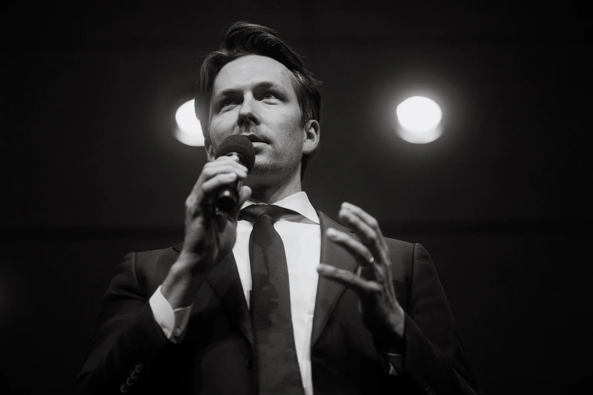 Speaker in a suit addresses the audience with a handheld microphone.