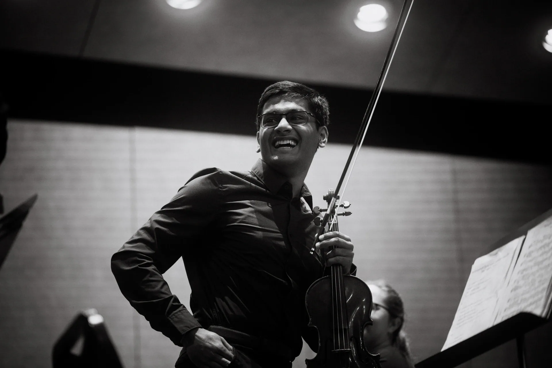 Violinist smiles while standing with violin and bow.