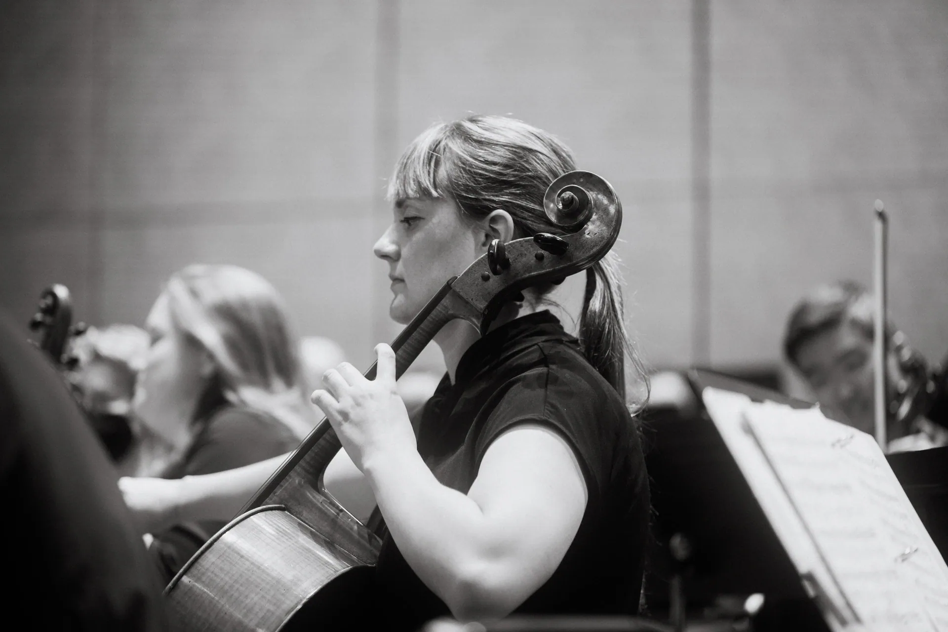 Cellist sits in profile with other string musicians behind.