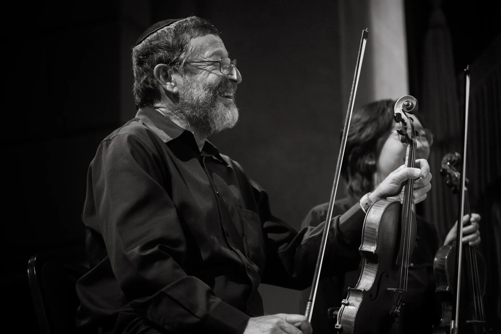 Smiling violinist sits holding a violin and bow.