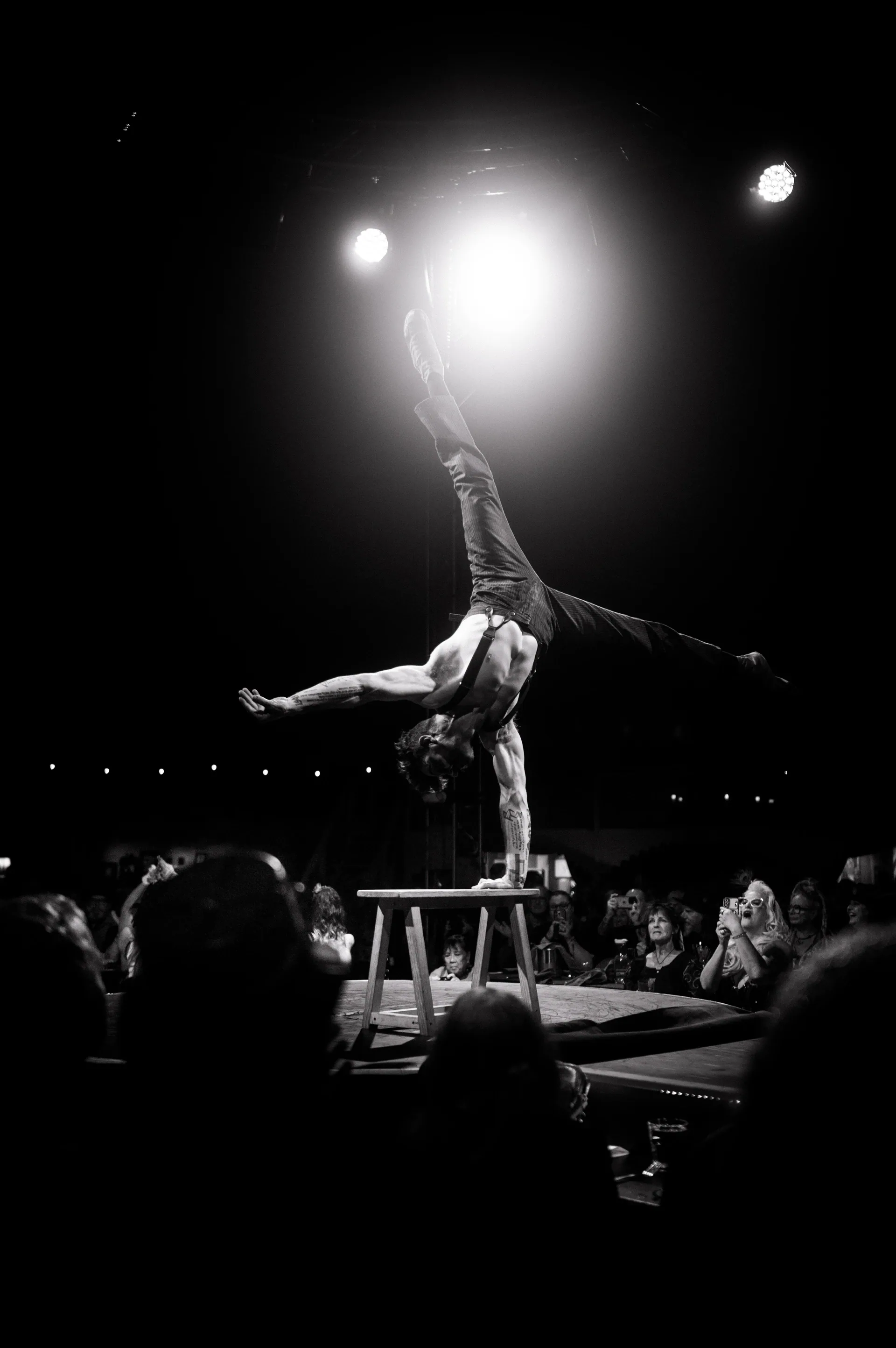 Performer balances on one hand atop a table with one leg raised vertically.