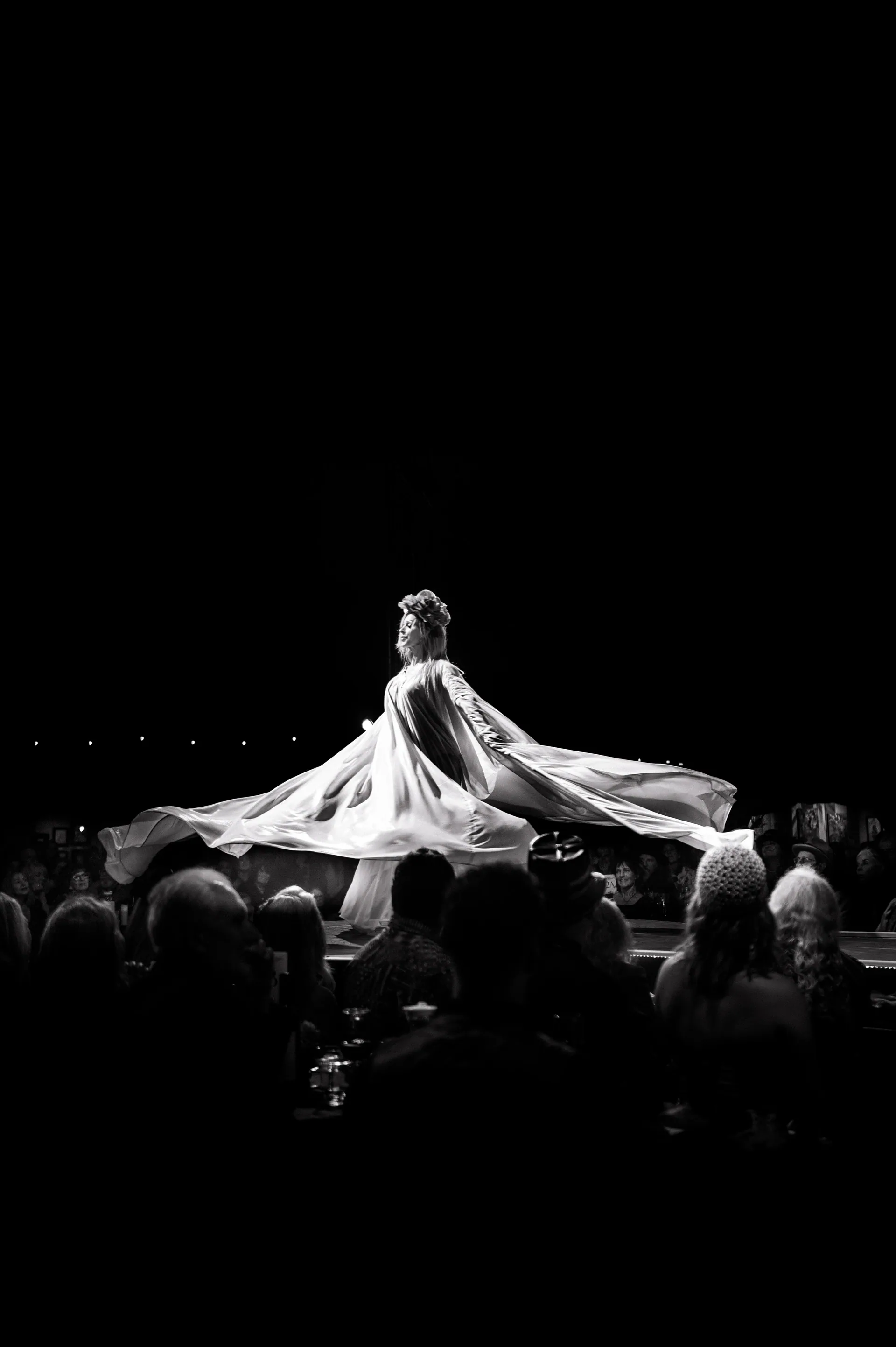 Performer spreads a broad cape across a circular stage surrounded by an audience.