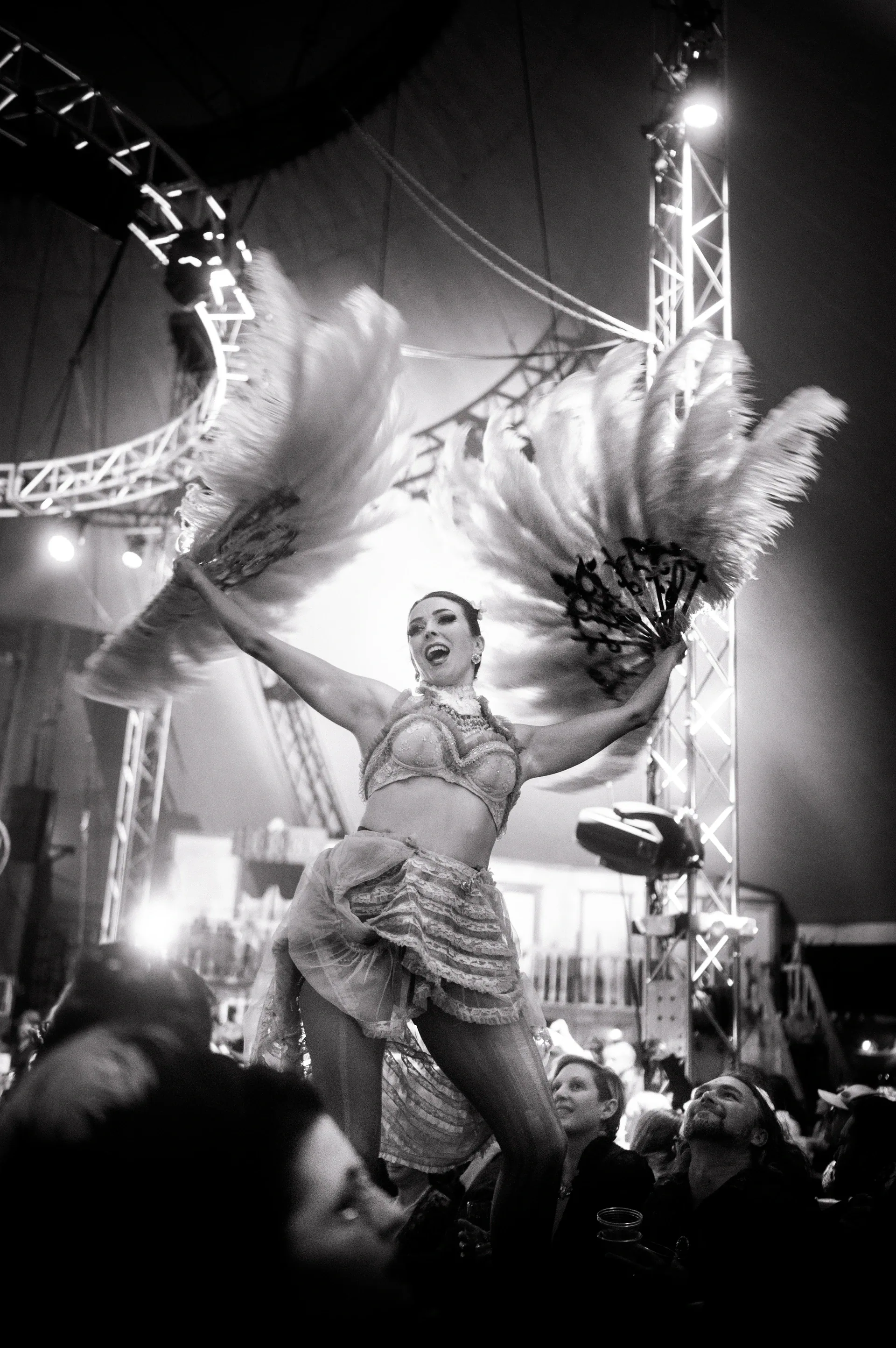 Performer in a feathered costume raises both arms beside the audience.