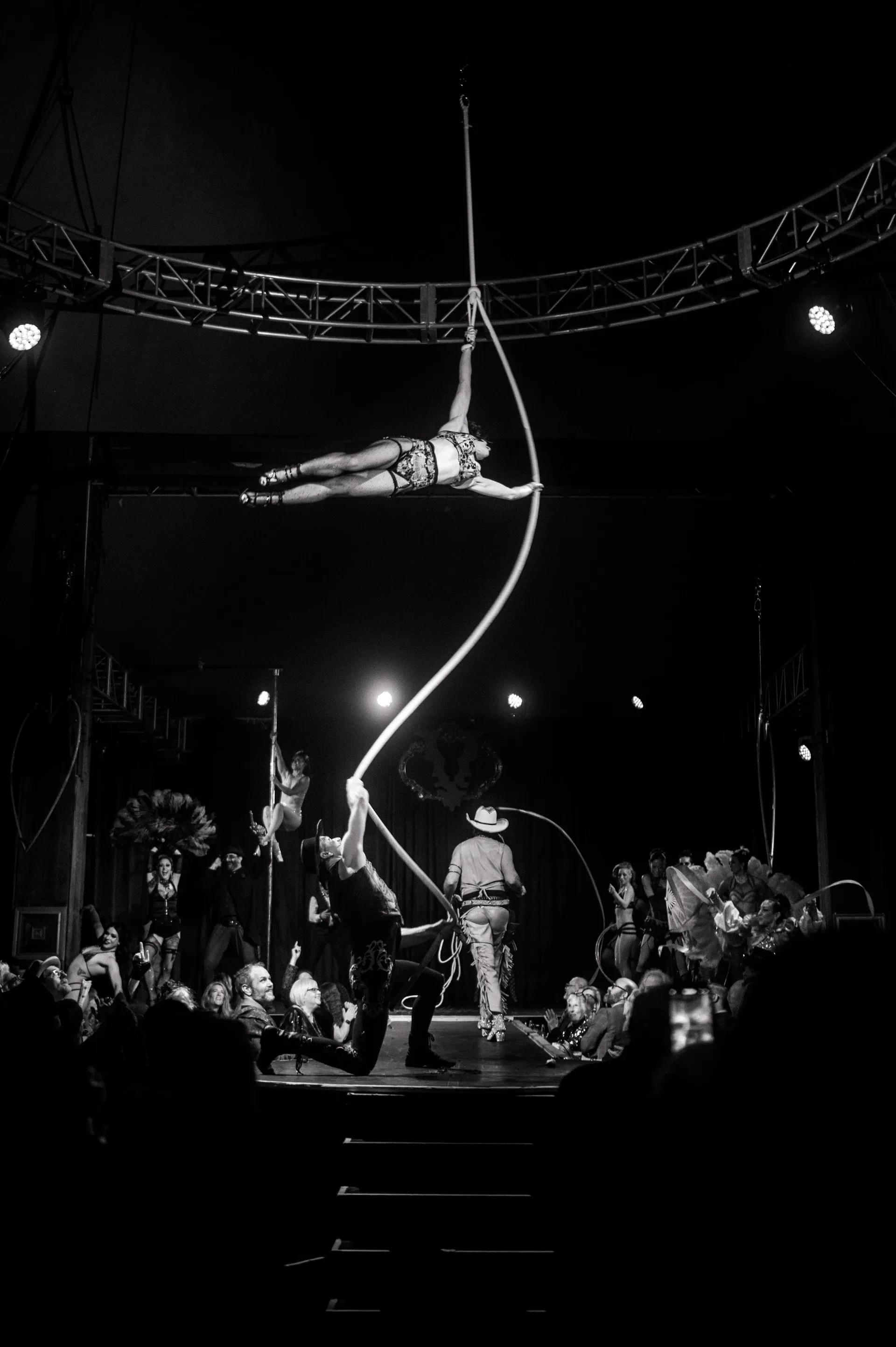 Aerialist extends horizontally from a curved suspended apparatus.