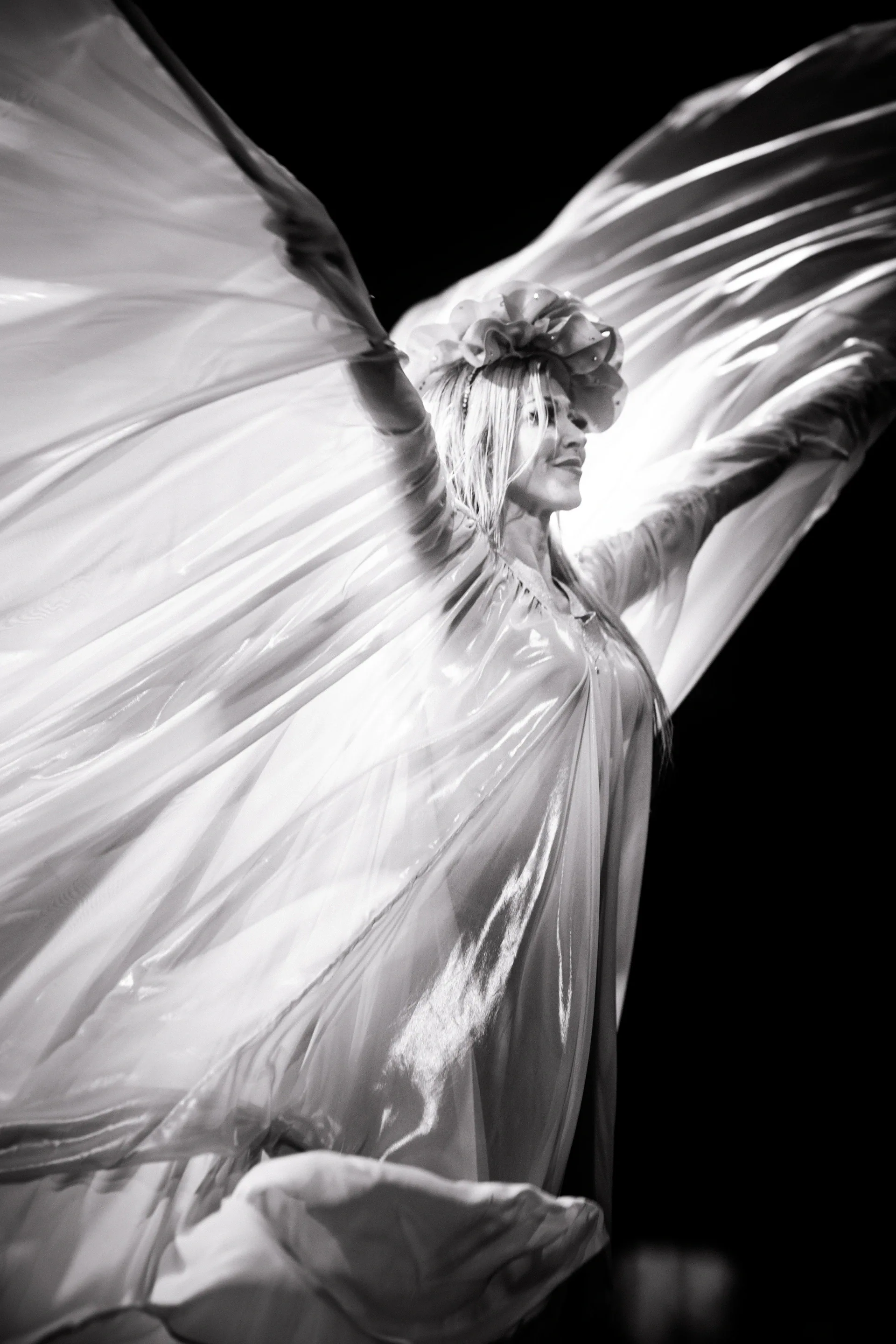 Performer sweeps a large sheet of fabric outward like wings.