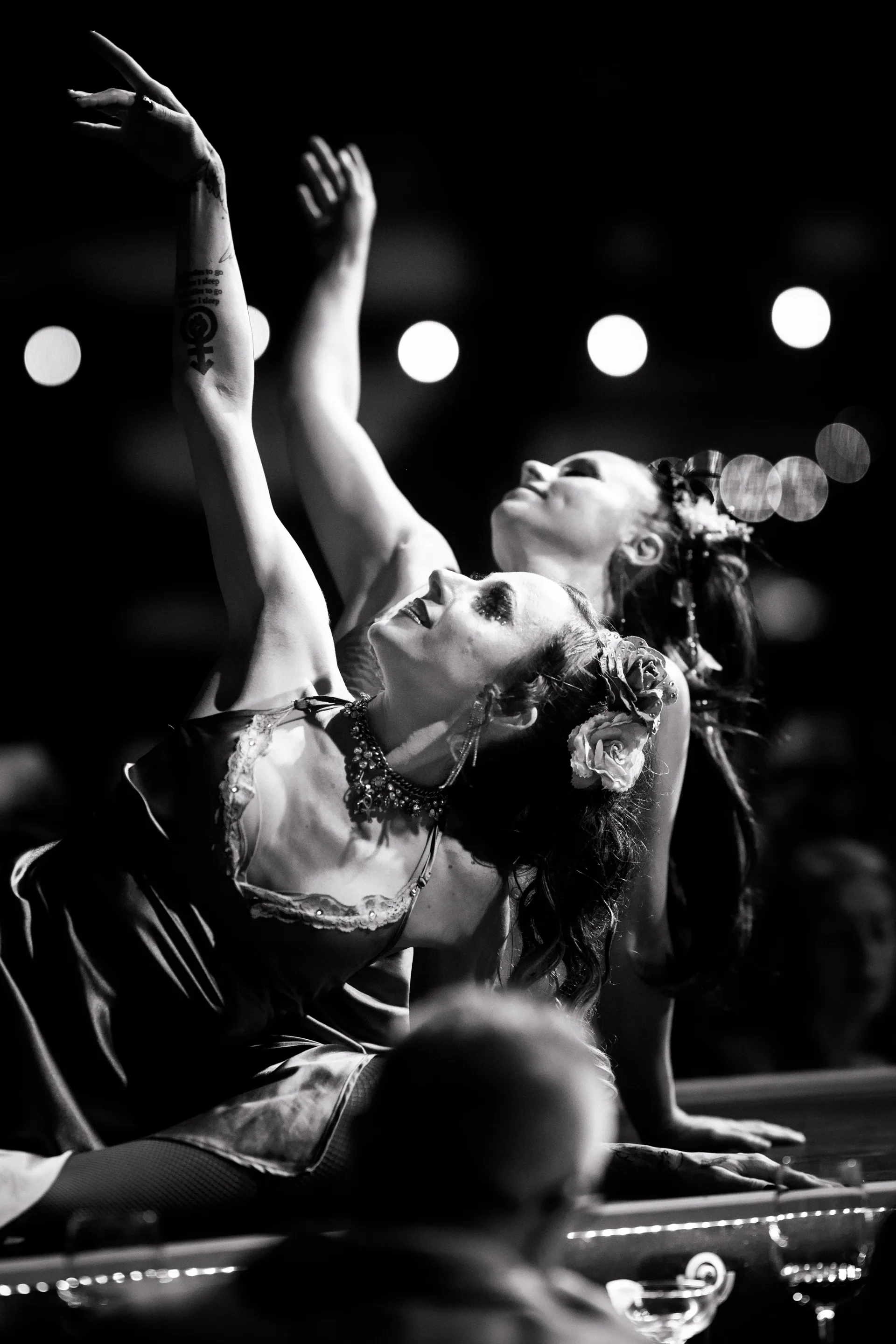 Performer in an ornate costume reclines onstage with arms and legs raised.