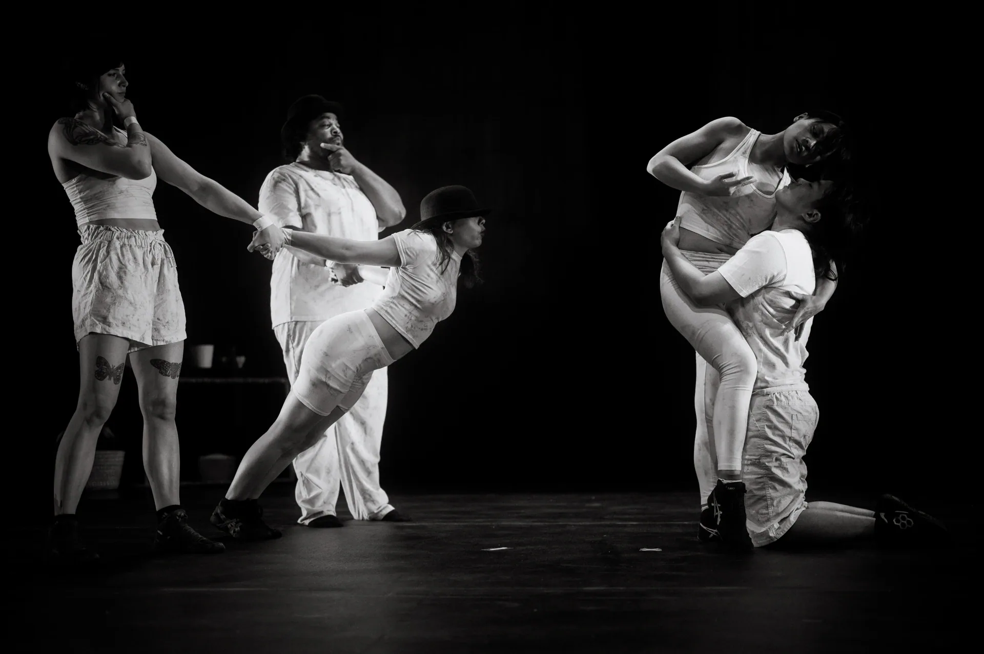 Four performers support and lean into one another across the stage.