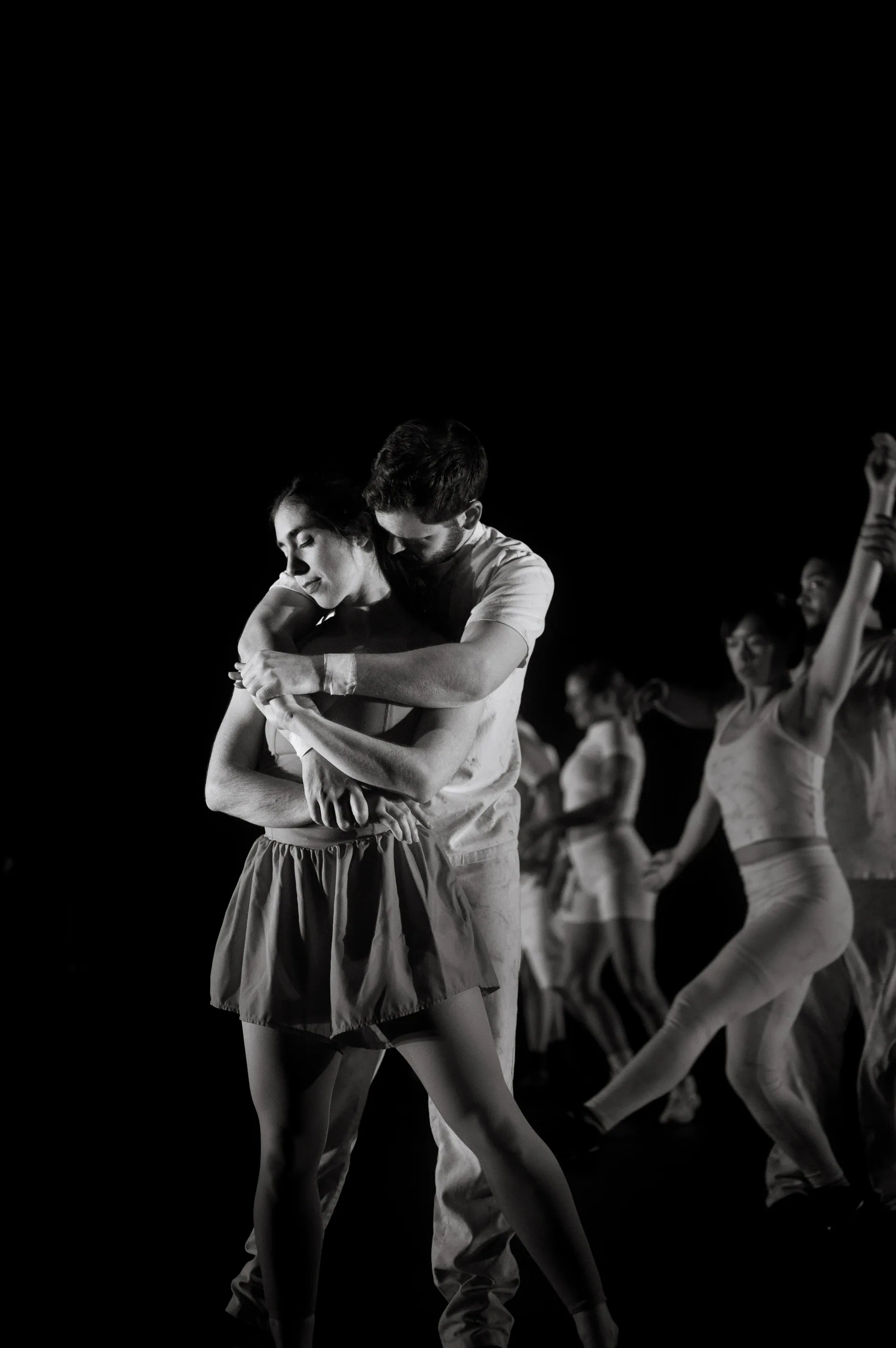 A central pair embraces while an ensemble moves behind them.