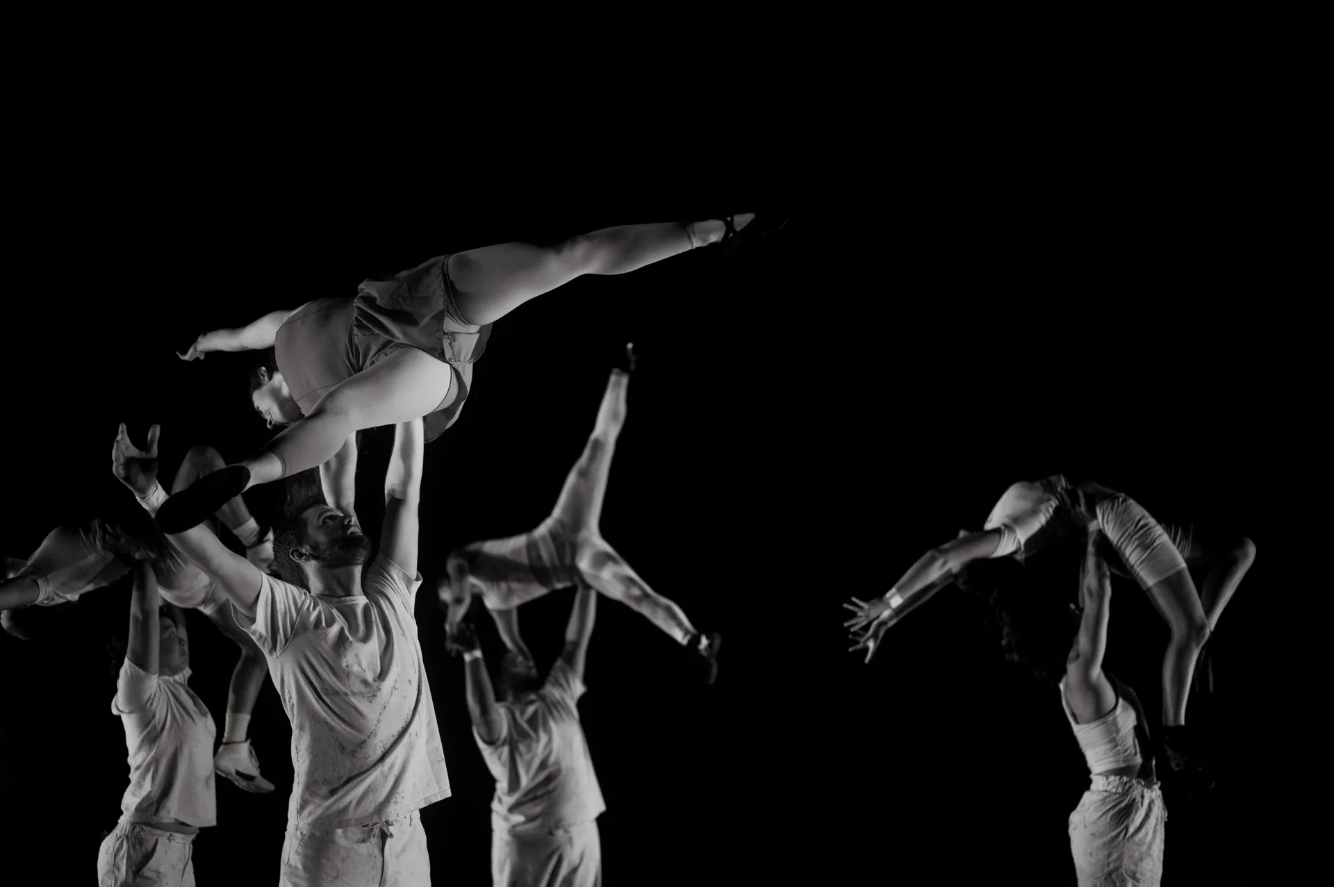 Ensemble lifts two performers horizontally above shoulder height.