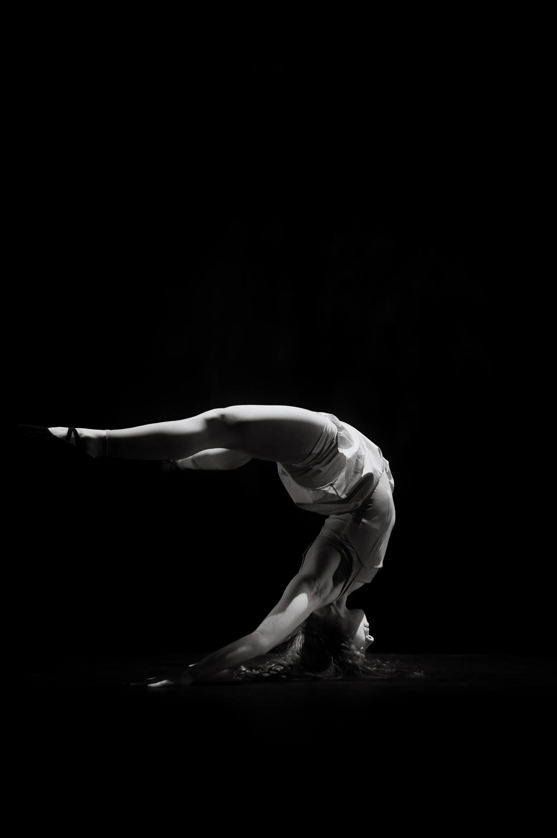 Solo performer holds a deep backbend on the stage.