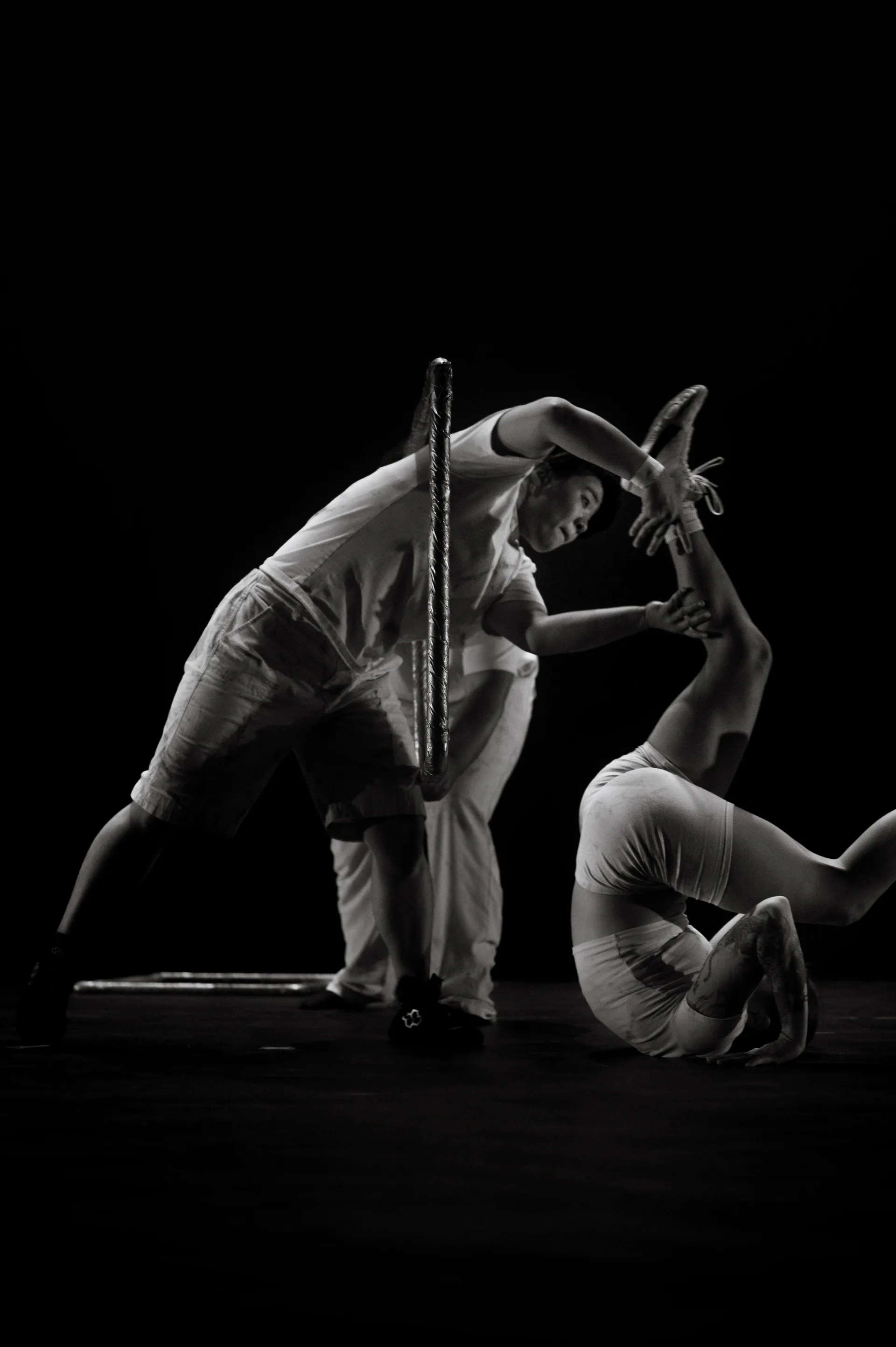 Two dancers move low to the stage with one bending over the other.
