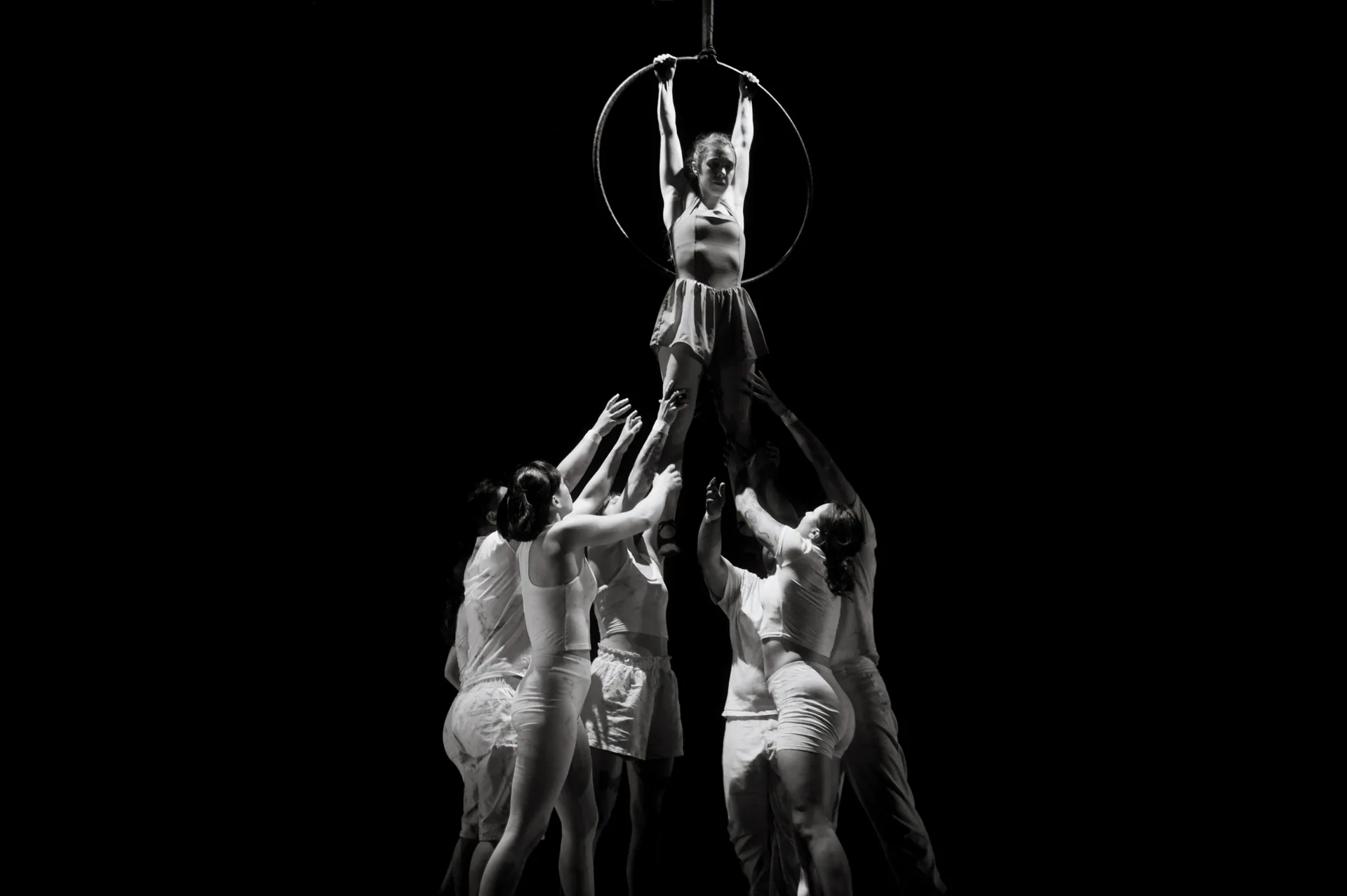 Ensemble lifts a performer upward into a suspended hoop.