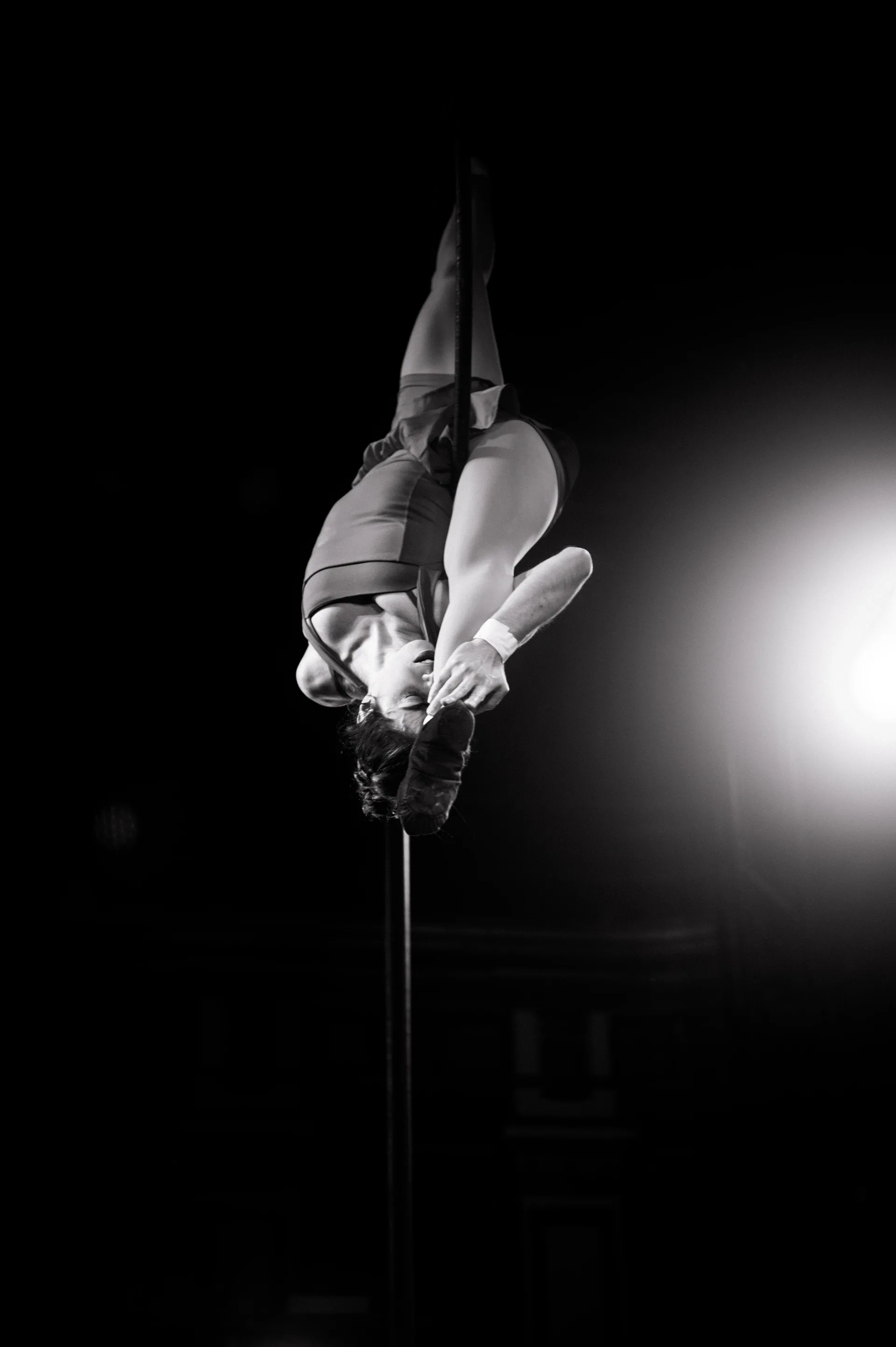 Aerialist hangs inverted from a vertical rope.