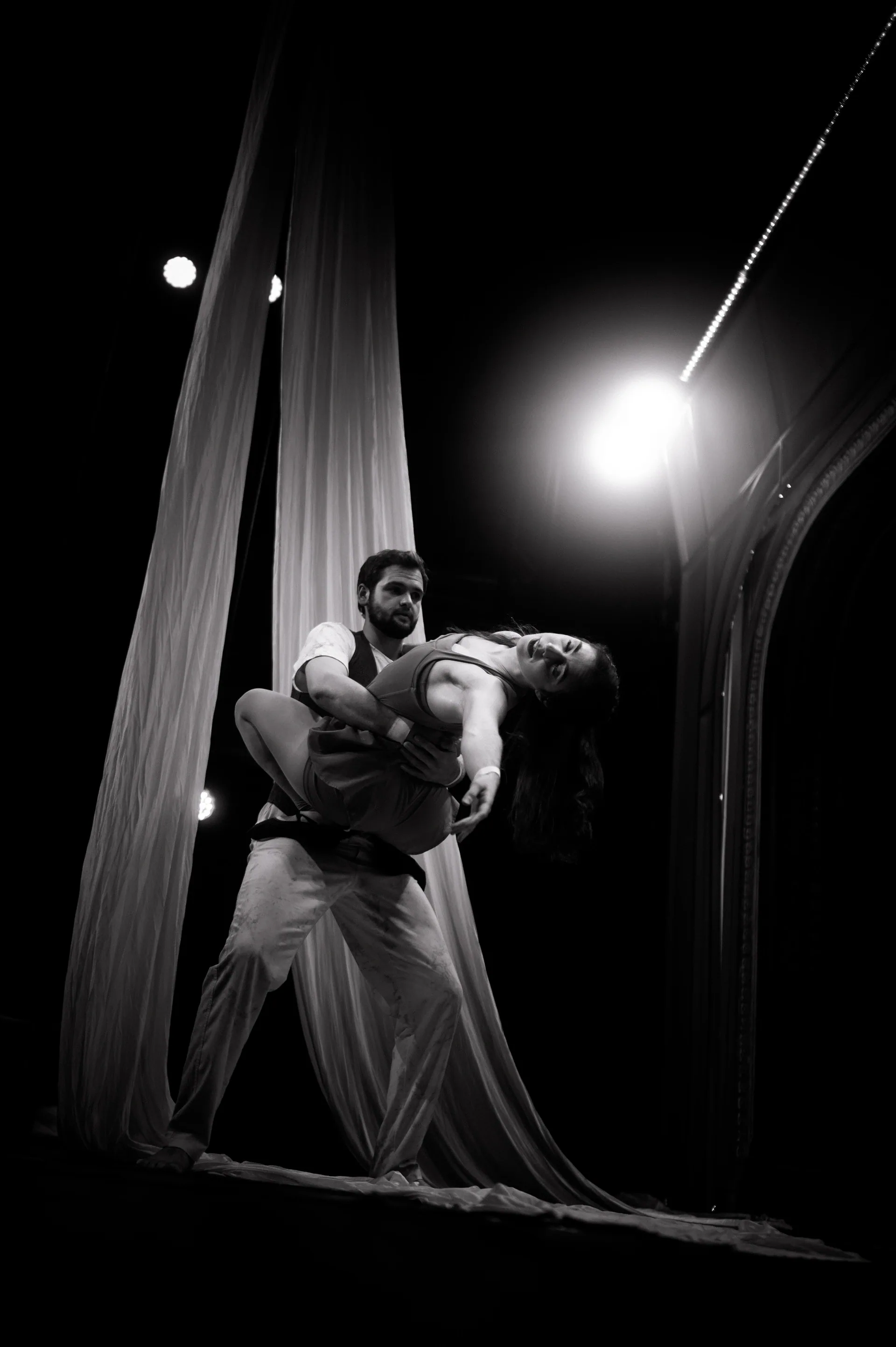 One performer carries another beside hanging fabric.