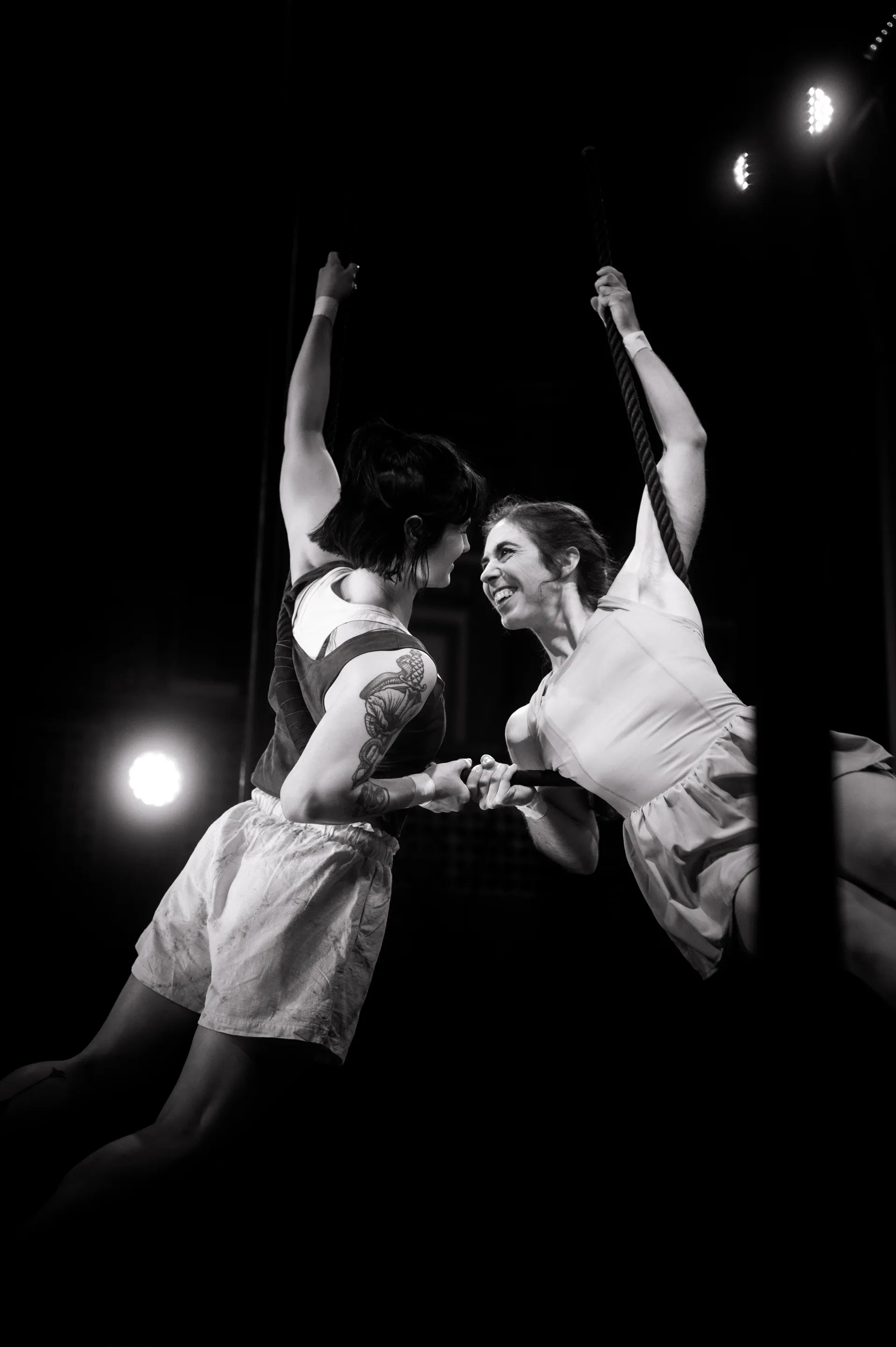 Two performers move across the stage with both arms raised.
