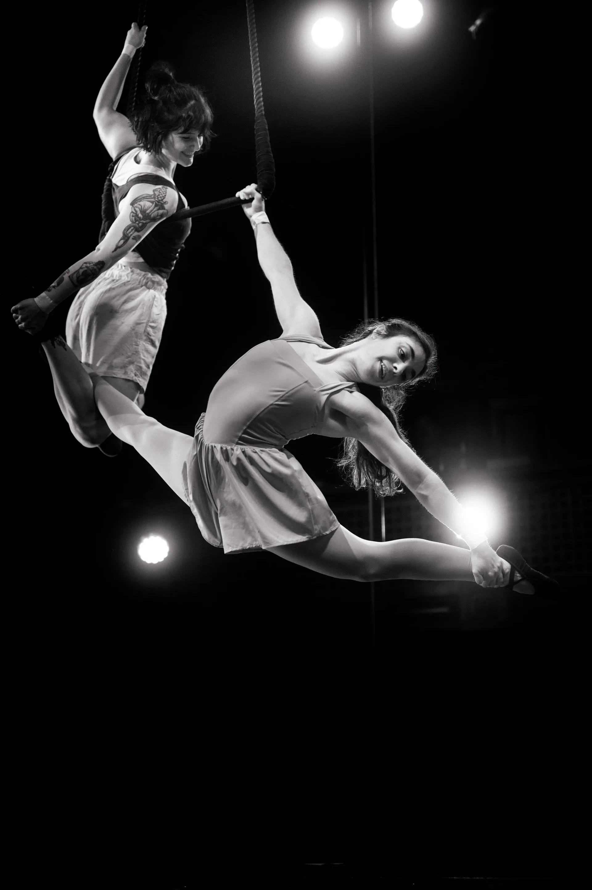 Two aerialists hang from the same rope while one extends outward.