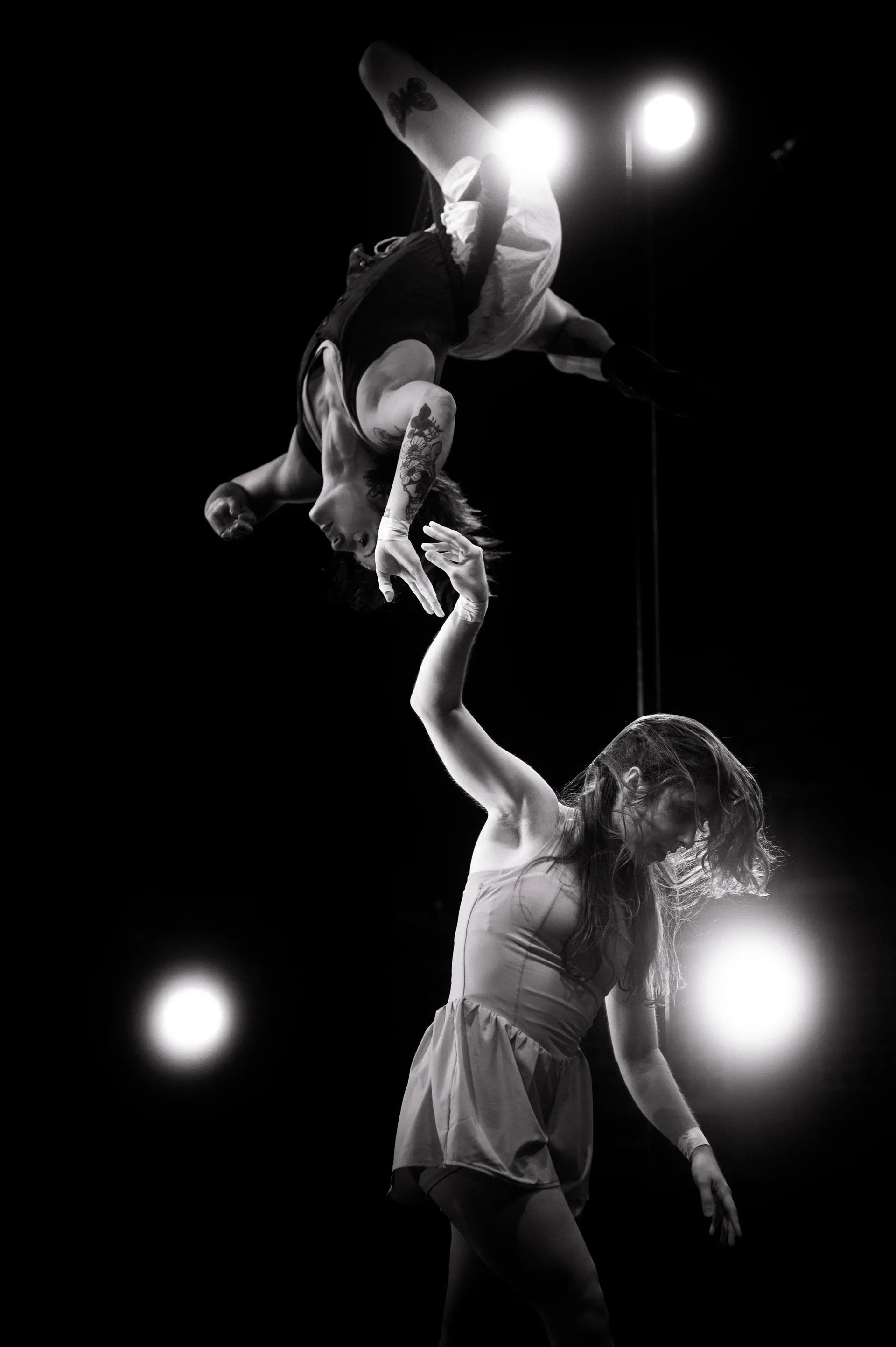 Standing performer reaches up toward an inverted acrobat overhead.