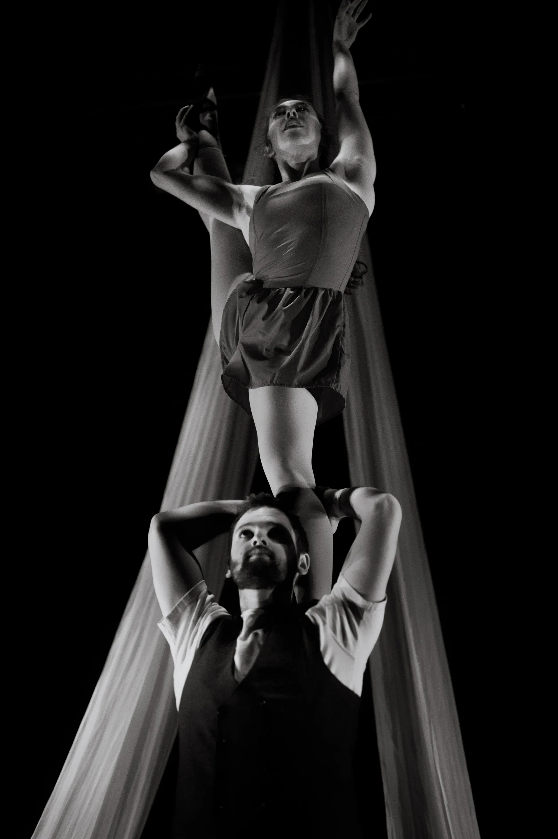 Aerialist sits in suspended fabric above a performer holding the trailing silk.